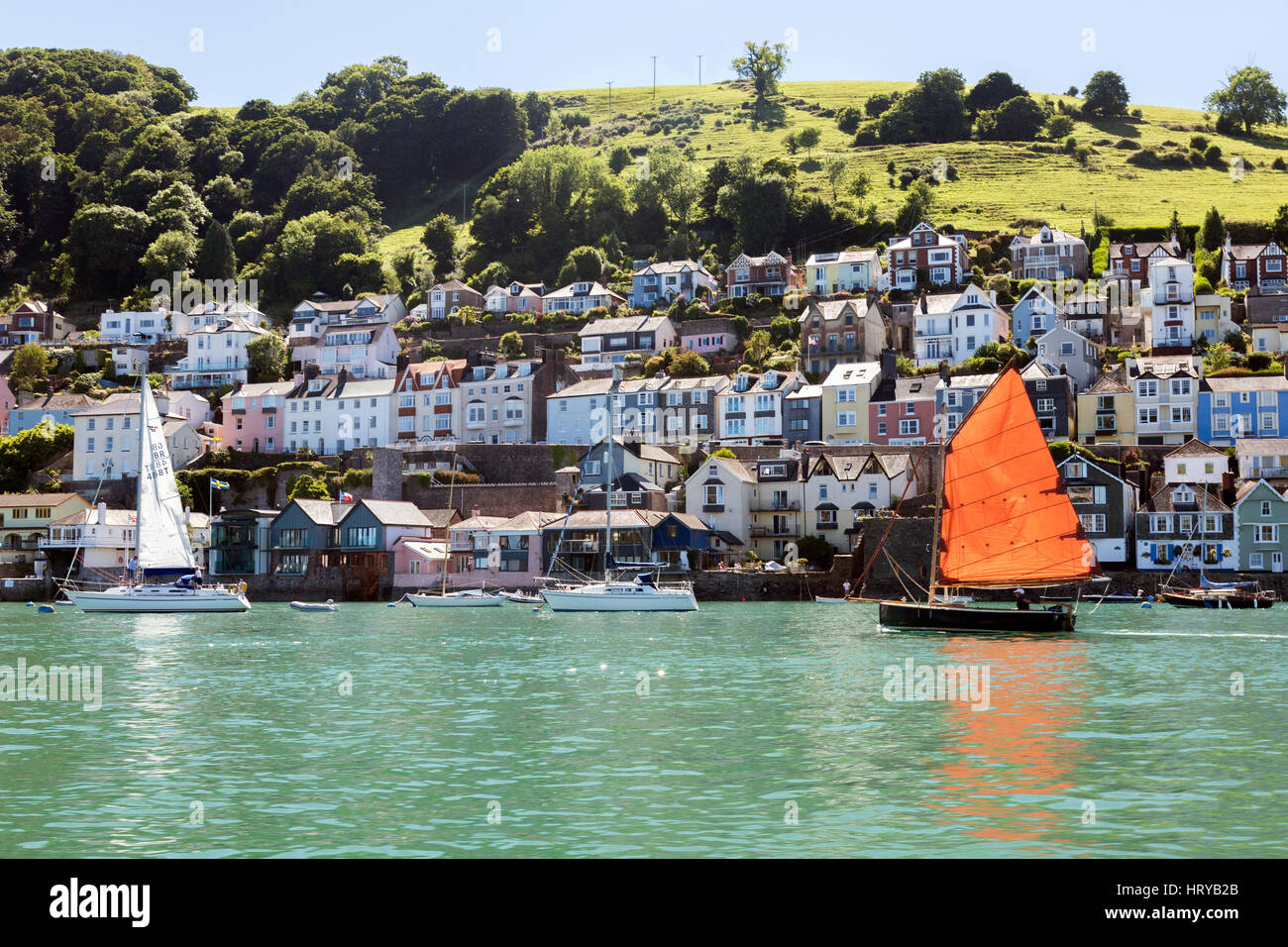 Eine Yacht mit hellen Segel macht seinen Weg nach unten der Fluss Dart vorbei an den Fluss vorderen Häusern in Dartmouth, Devon, England, UK Stockfoto