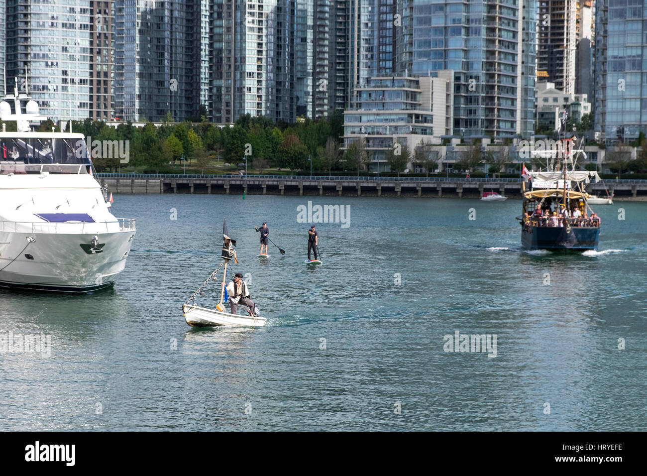 Ein Mann gekleidet wie ein Pirat in ein weißes Boot mit einem großen schwarzen Boot mit Segel nach unten und zwei Personen auf Paddel-gejagt wird. False Creek, Vancouver, BC. Stockfoto