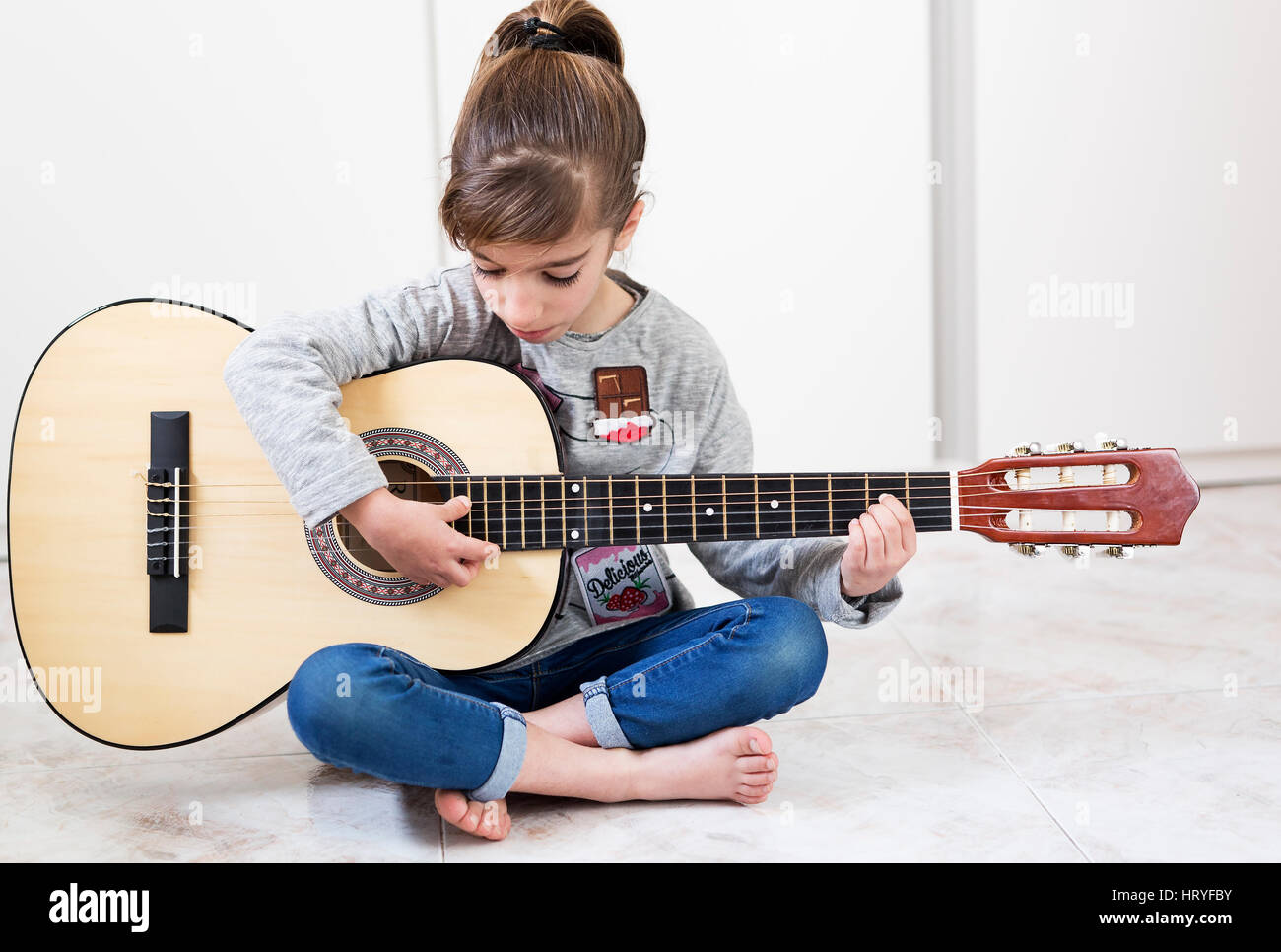 9 Jahre altes Mädchen lernen, Gitarre zu spielen. Horizontal mit Lichteinfall durch ein Fenster geschossen. Stockfoto