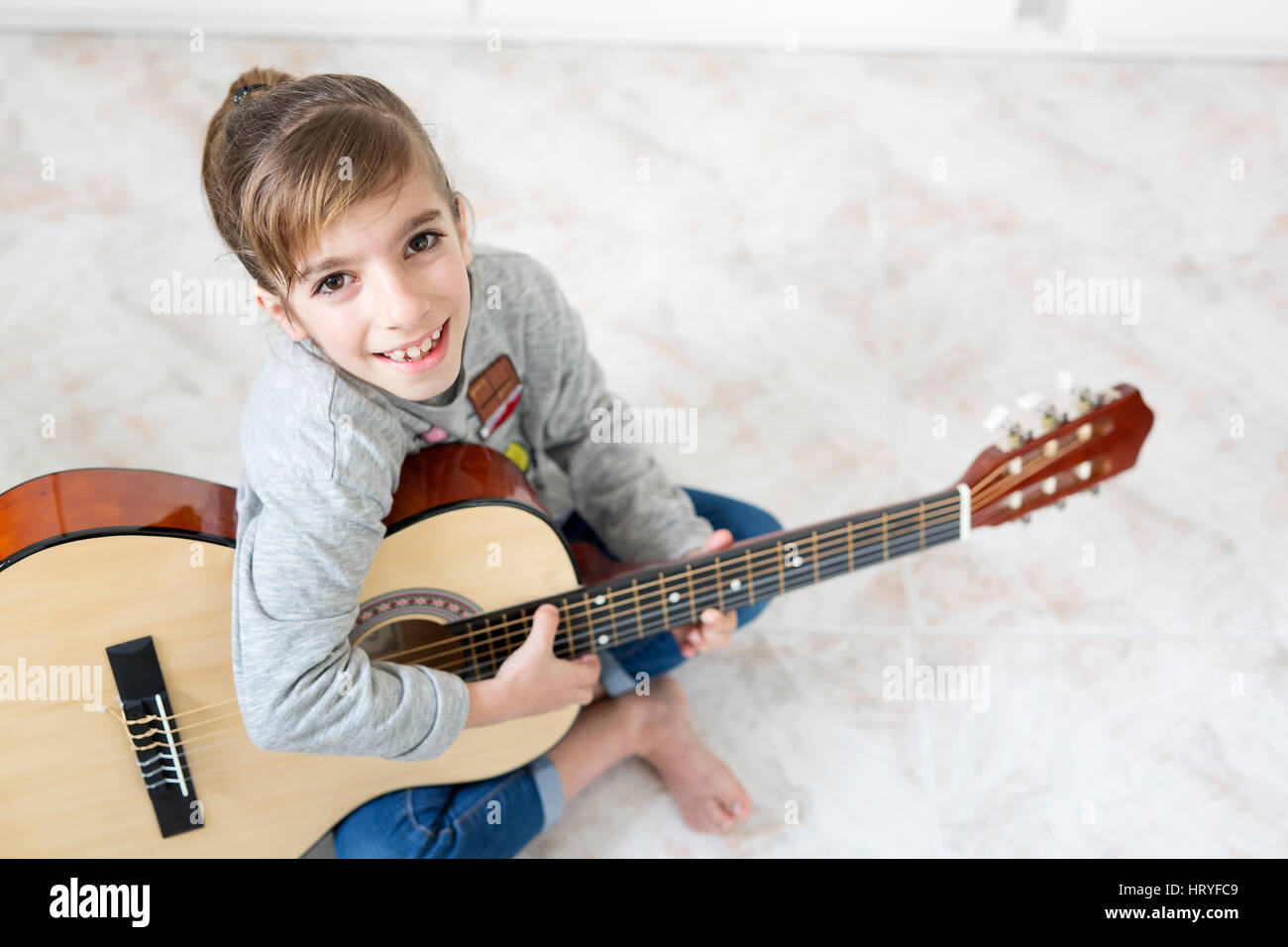 9 Jahre altes Mädchen lernen, Gitarre zu spielen. Horizontal mit Lichteinfall durch ein Fenster geschossen. Stockfoto