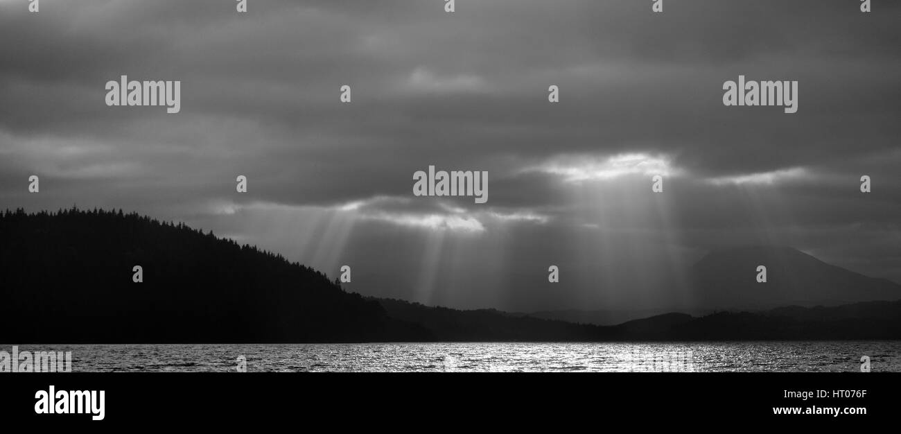 Sonnenstrahlen durchdringen dunkle Wolken über Loch Garry und dichten Nadelwaldflächen, Lochaber, Schottland, September 2016. Stockfoto