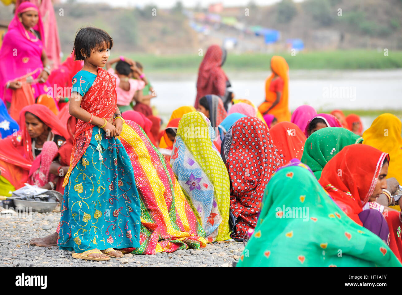 Eine junge Rajasthani Mädchen in einer lebendigen bestickt traditionelles Kleid steht unter einer Gruppe von sitzenden Frauen Stockfoto