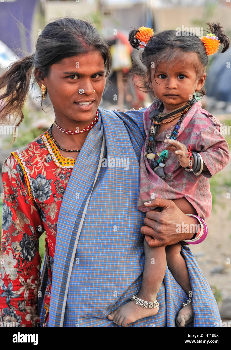 Eine junge Rajasthani Mutter Kleider ihren kleinen Sohn als kleines Mädchen Stockfoto