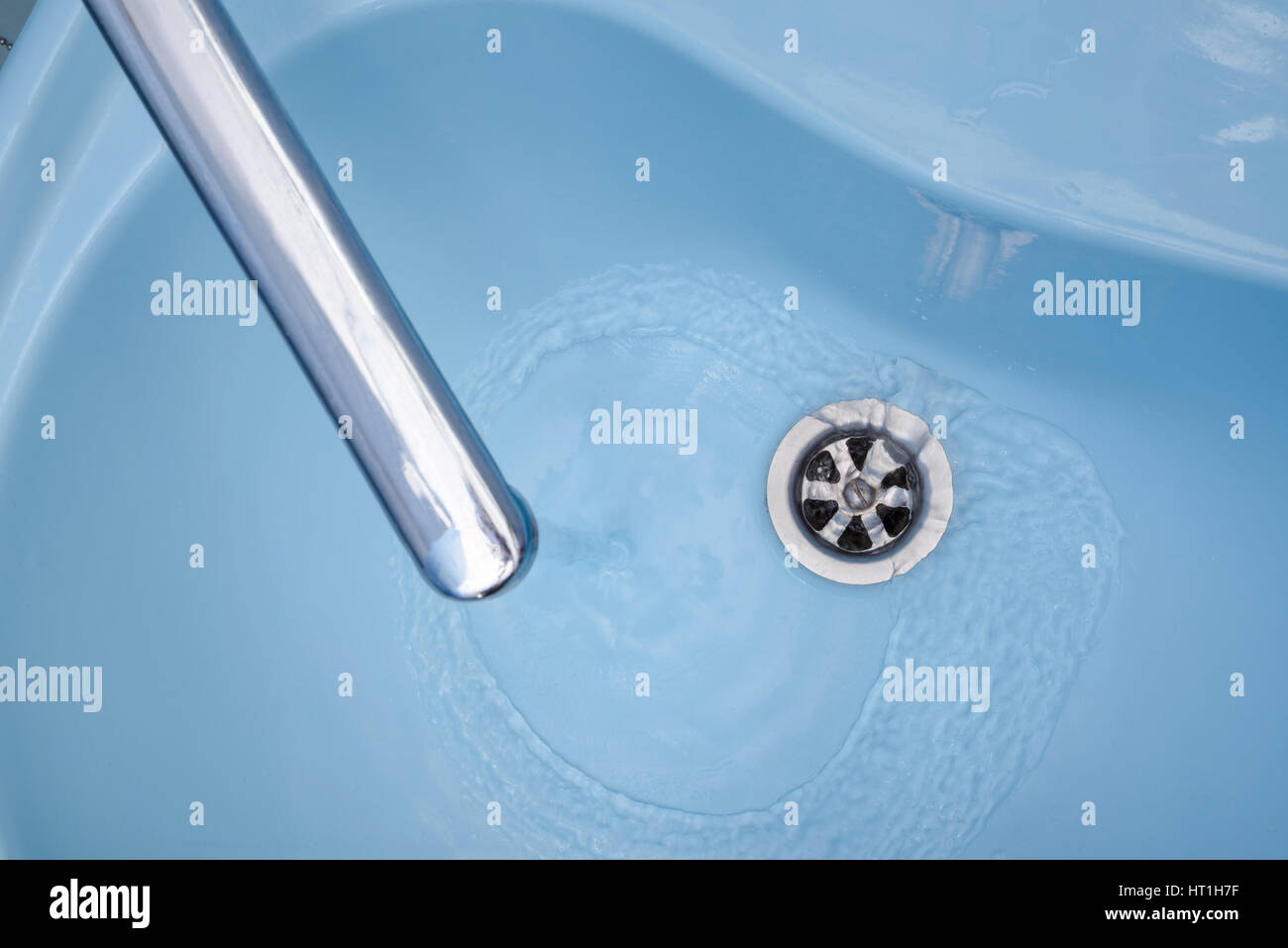 Das Wasser fließt aus dem Hahn in einem blauen Waschbecken. Die Flüssigkeit gießt, wirbelnden, in den offenen Stecker Stockfoto