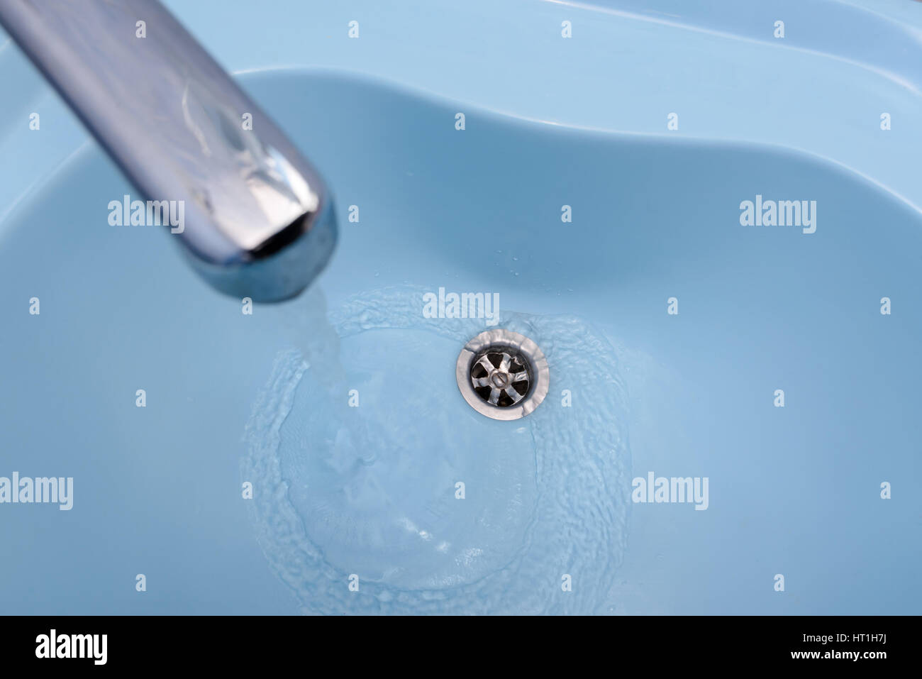 Das Wasser fließt aus dem Hahn in einem blauen Waschbecken. Die Flüssigkeit gießt, wirbelnden, in den offenen Stecker Stockfoto