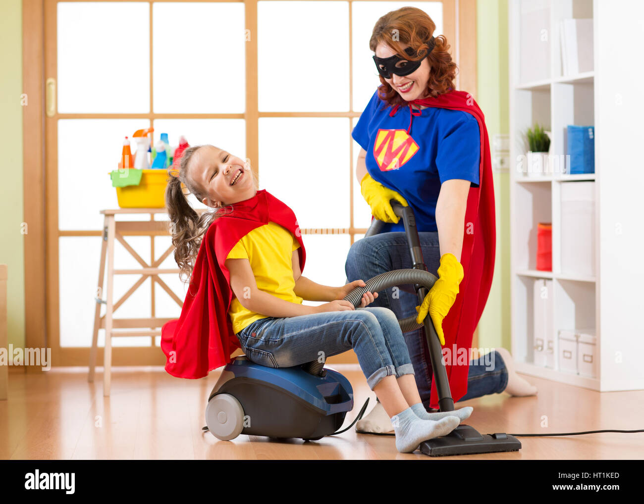 Superhelden kid Mädchen und ihre Mutter Wäsche zusammen im Wohnzimmer. Familie - im mittleren Alter Frau und Kind Tochter haben Spaß beim Staubsaugen Stockfoto