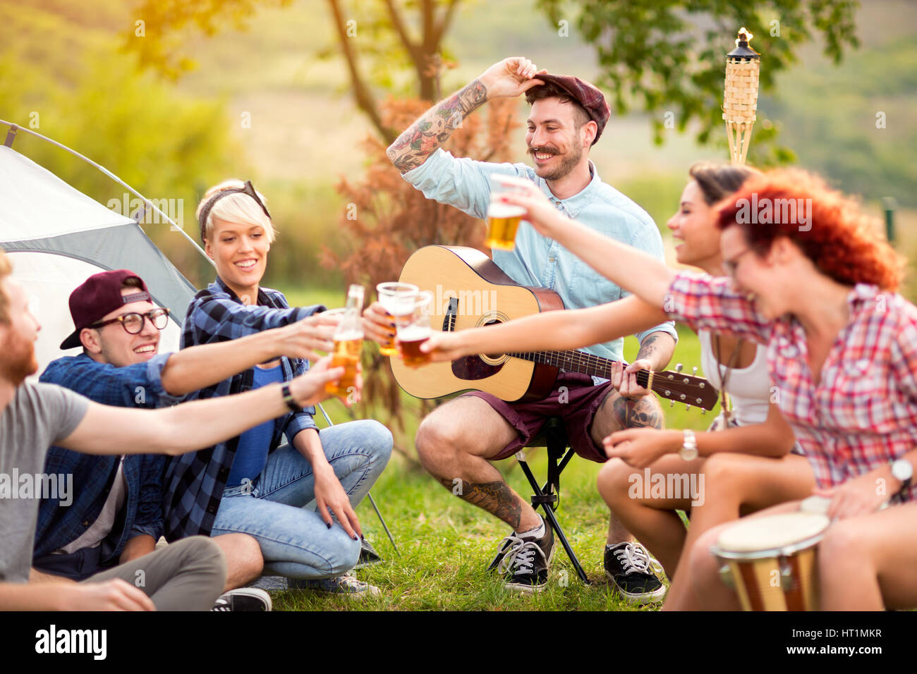 YJoyous Jugendliche Klopfen mit Glas Bier im Camp auf unter freiem Himmel Stockfoto