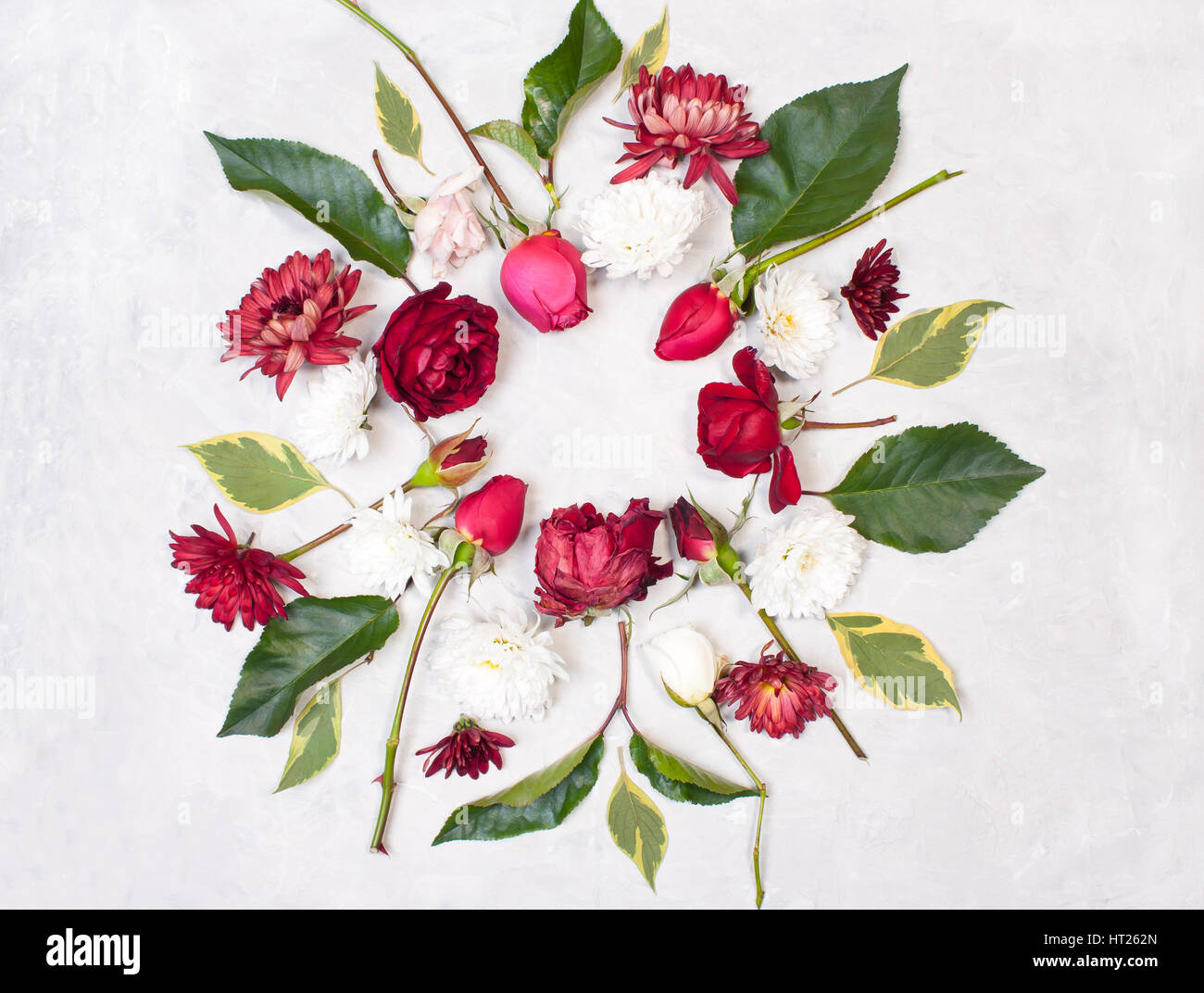 Runde Rahmen aus Blumen. Dekorationen von roten Rosen, Knospen, grüne Blätter und weiße Chrysanthemen auf grauem Beton Hintergrund. Ansicht von oben flach Stockfoto