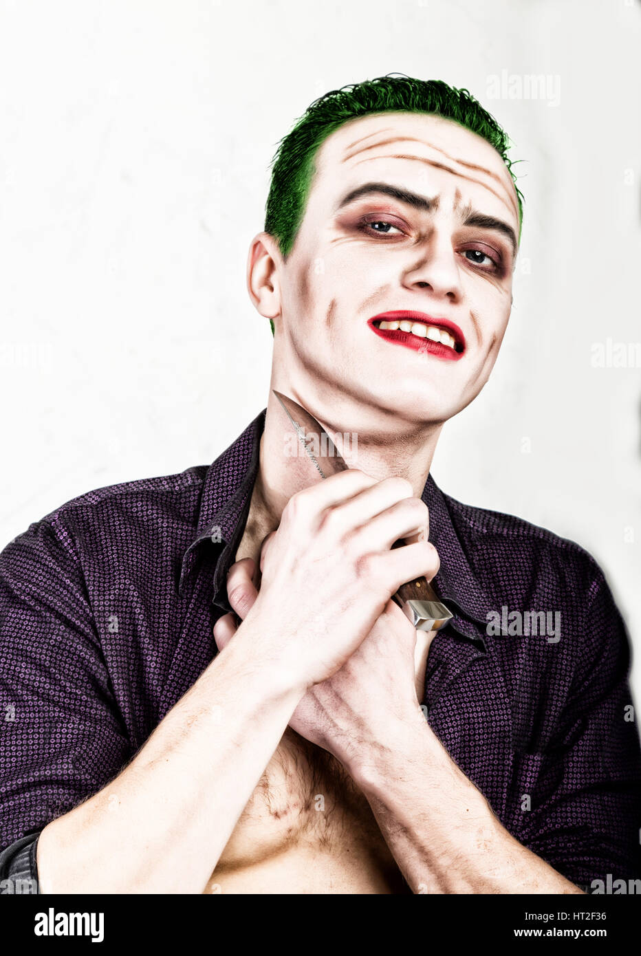 Kerl mit verrückten Joker Gesicht halten, Messer, grüne Haare und idiotische Smike. Karneval Kostüm. Stockfoto