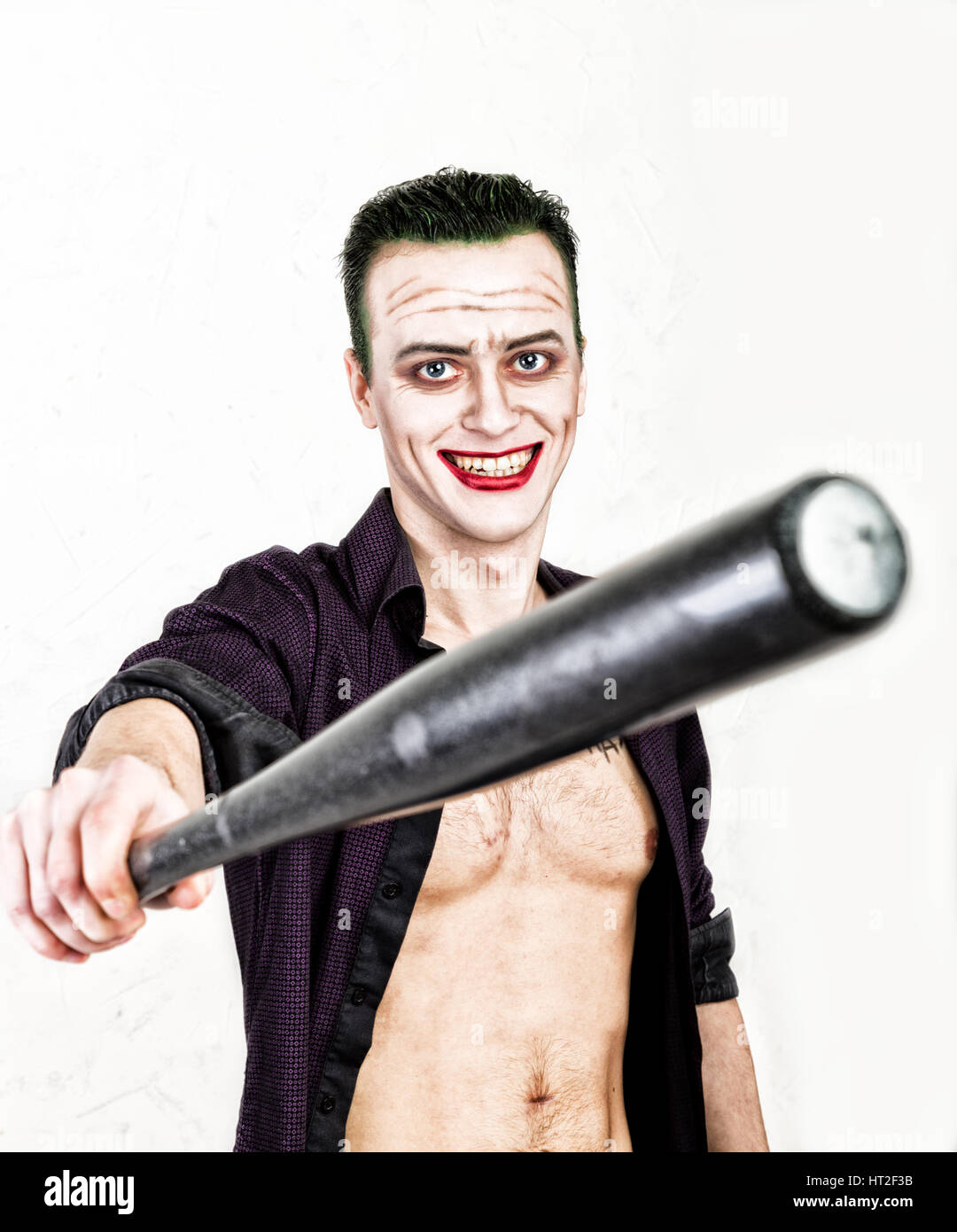Kerl mit verrückten Joker Gesicht halten, Baseballschläger, grüne Haare und idiotische Smike. Karneval Kostüm. Stockfoto