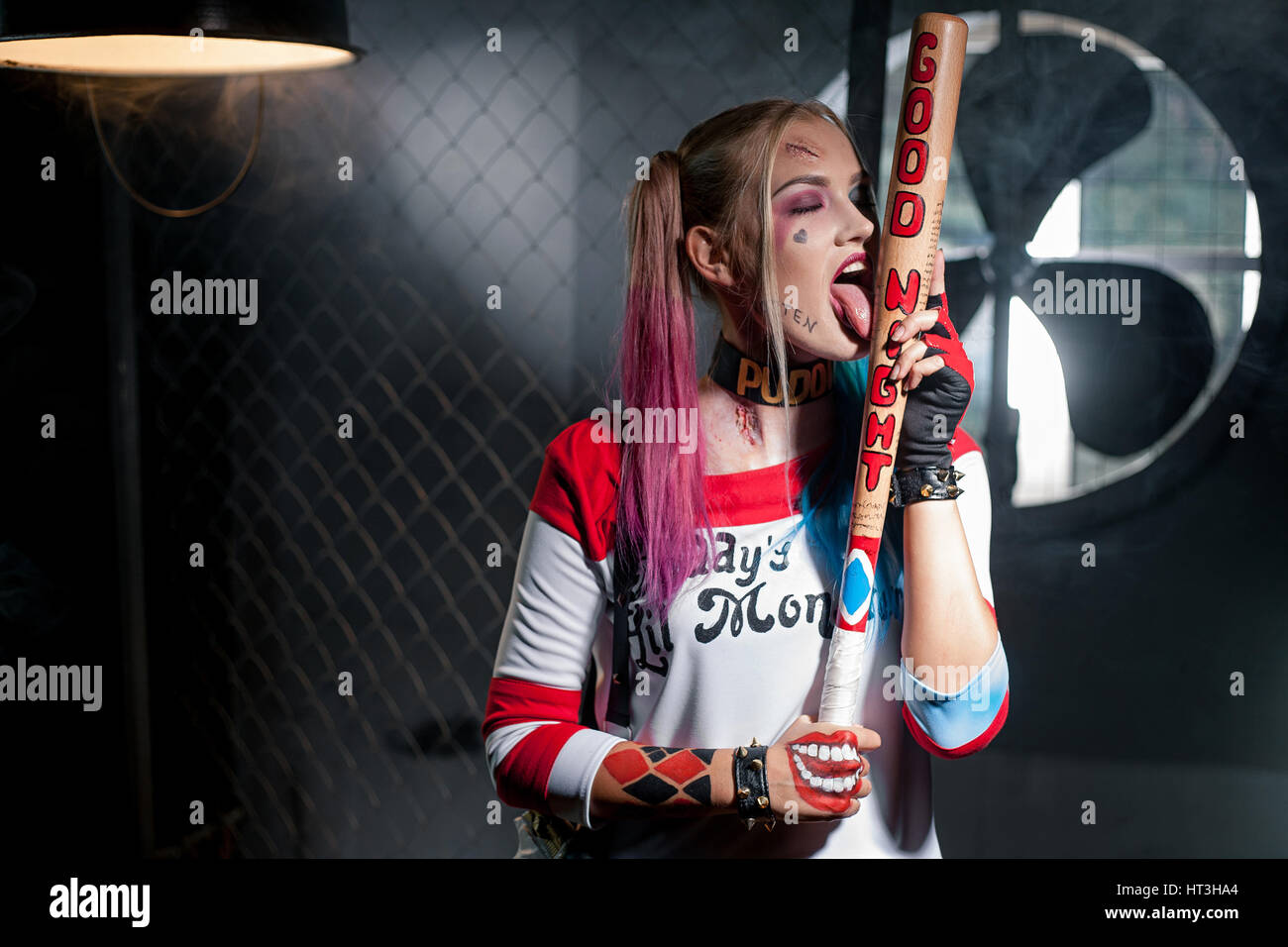 Mädchen in Tracht Harley Quinn. Sie steht mit einem Schläger und leckt ihre  Fledermaus. Hautnah. Cosplay Stockfotografie - Alamy