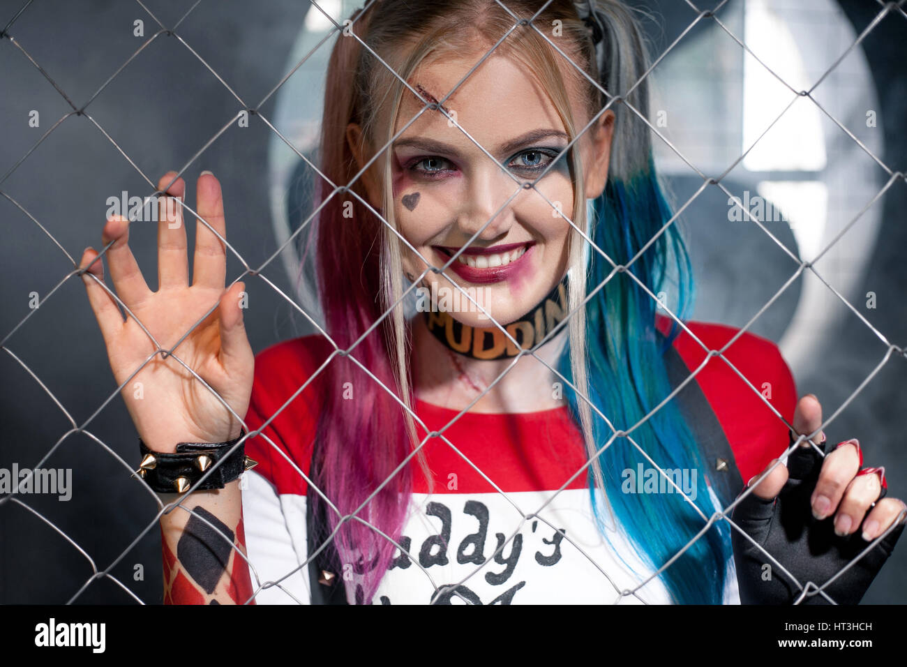 Porträt der lächelnde Mädchen in Tracht Harley Quinn. Sie schaut durch das Gitter. Hautnah. Cosplay. Stockfoto