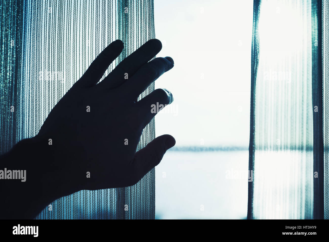 Männliche Hand öffnet Tüll am Fenster mit hellem Tageslicht draußen, blau getönten Foto Stockfoto