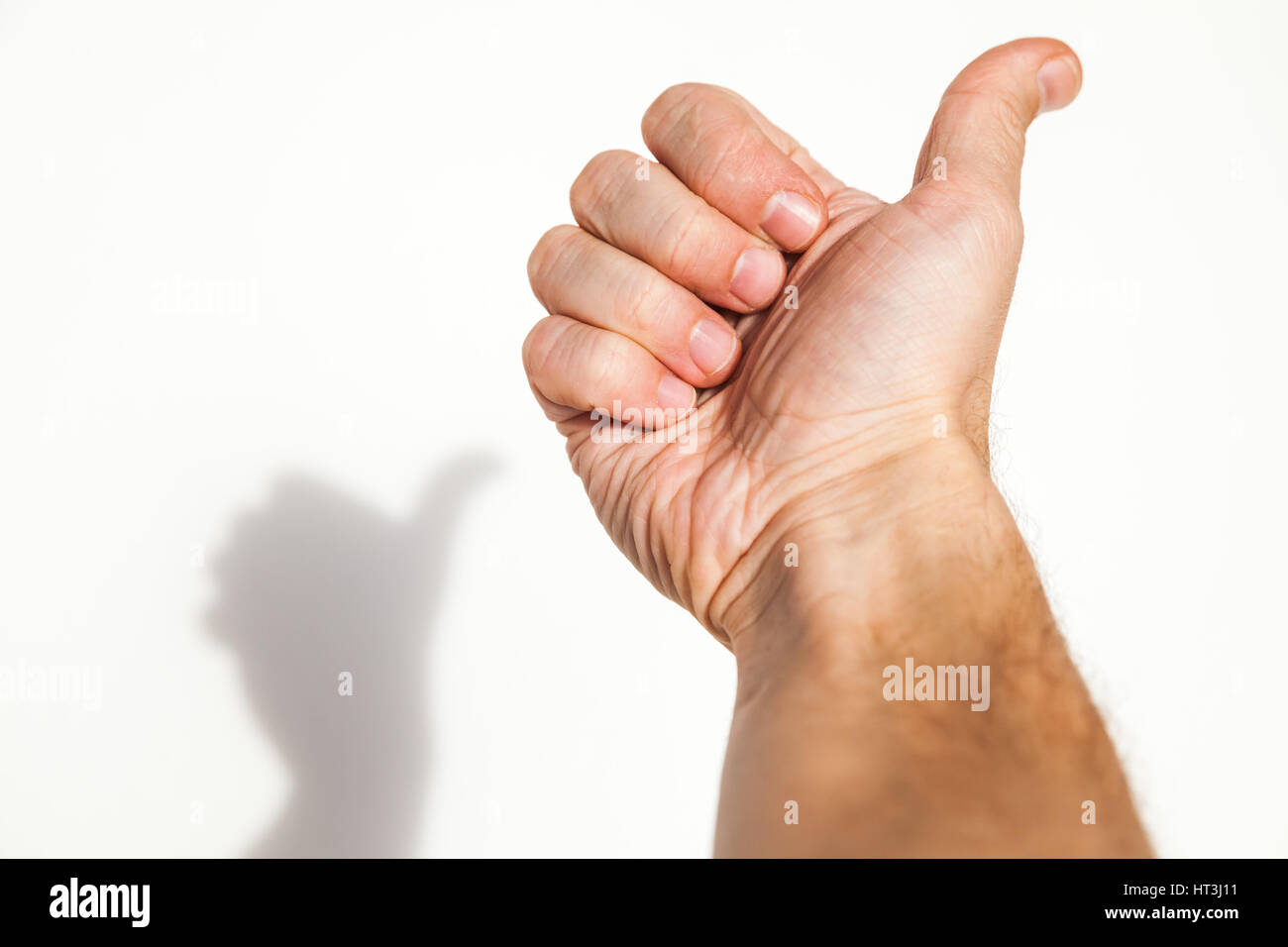 Männliche Hand zeigt Daumen hoch Geste auf weiße Wand Hintergrund mit weichen Schatten, wie es Konzept Stockfoto