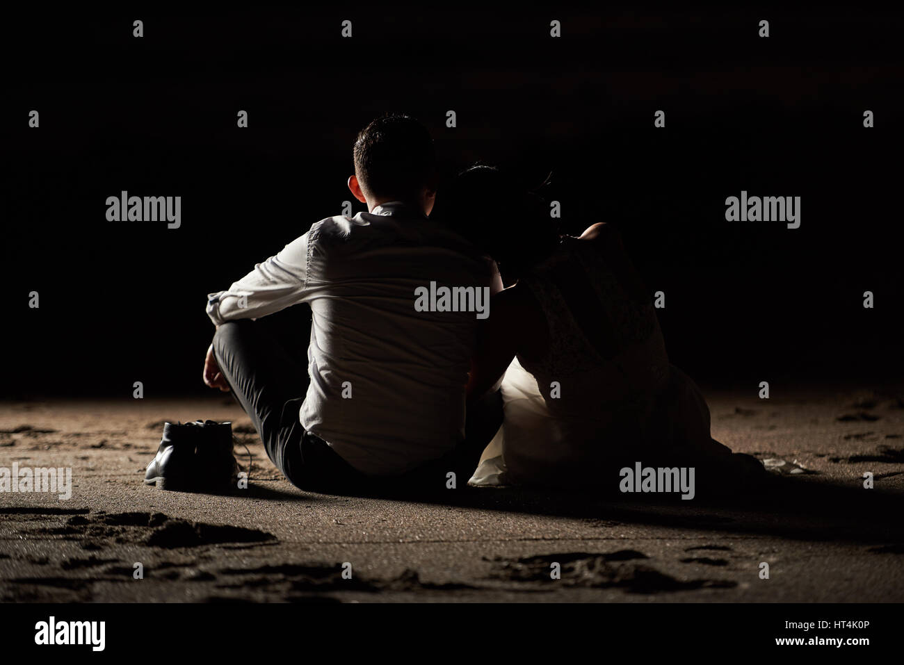 Bräutigam und die Braut sitzt auf Strandsand Blick von hinten. Brautpaar sitzen auf Sand auf schwarzem Hintergrund isoliert Stockfoto