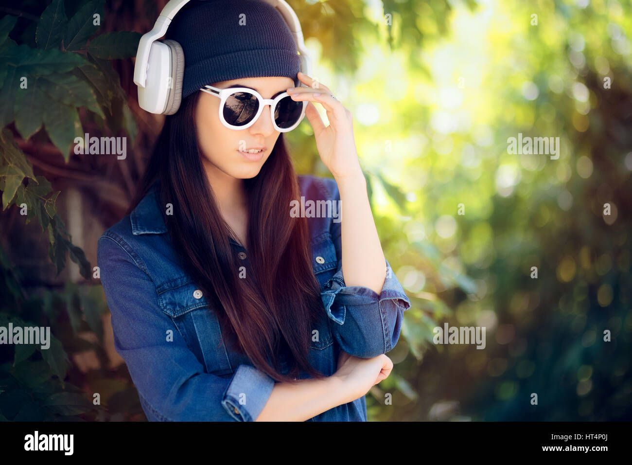 Denim Fashion Girl mit Sonnenbrille anhören von Musik über Kopfhörer Stockfoto