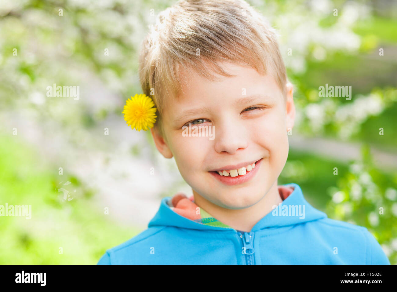 Closeup Portrait von niedlichen lustige kleine Junge über grüne blühende Bäume Hintergrund isoliert. Kaukasische blonde Kind genießen sonniges warmes Wetter im Frühjahr Stockfoto