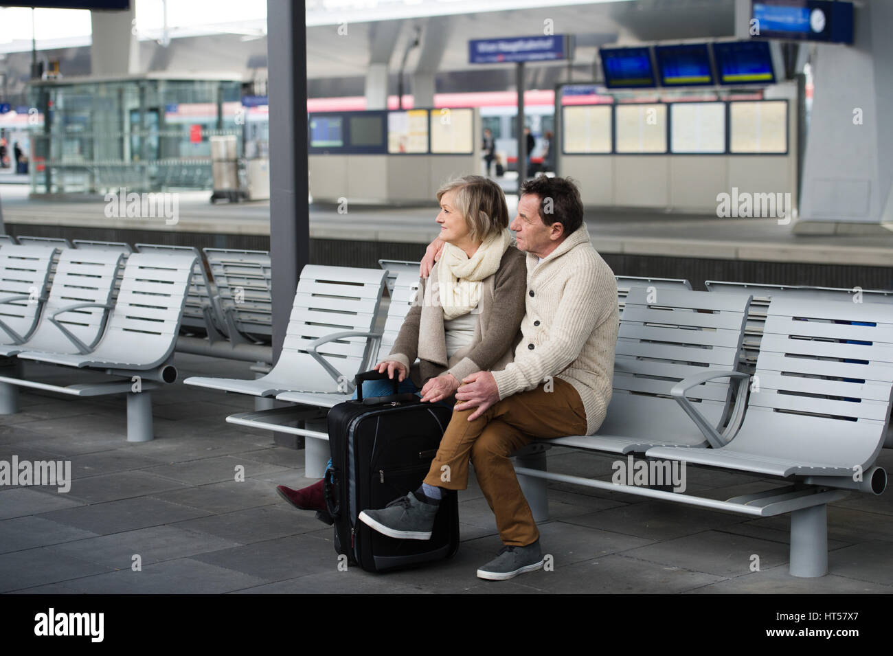 Schönes älteres paar warten am Bahnhof, auf Bank sitzend, mit Blick auf die Uhr. Stockfoto