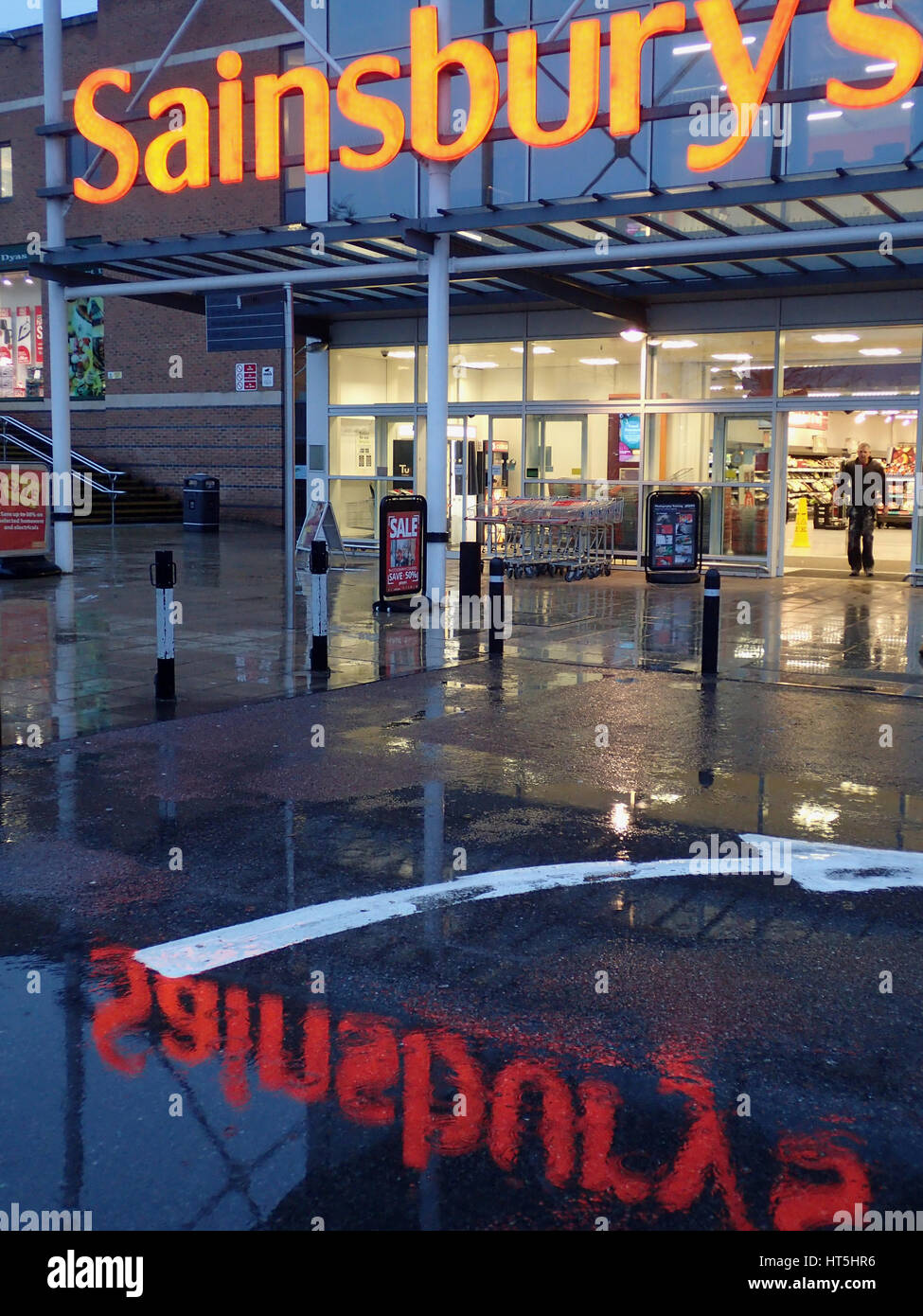 Der Eingang des Didcot Sainsbury im Regen mit dem Sainsbury Zeichen spiegelt sich in einer Pfütze vor dem Eingang in vollem Umfang Stockfoto