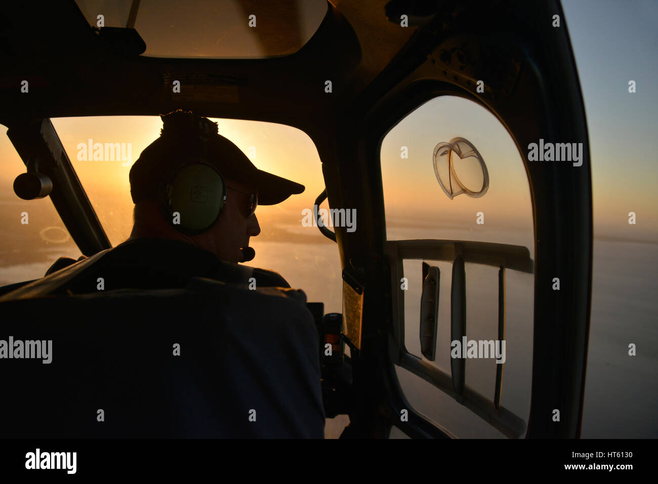 Ein Luftschuss des Innenraums eines Hubschraubers vom Typ Eurocopter AS350 mit Pilot-Silhouetten gegen die untergehende Sonne. Stockfoto