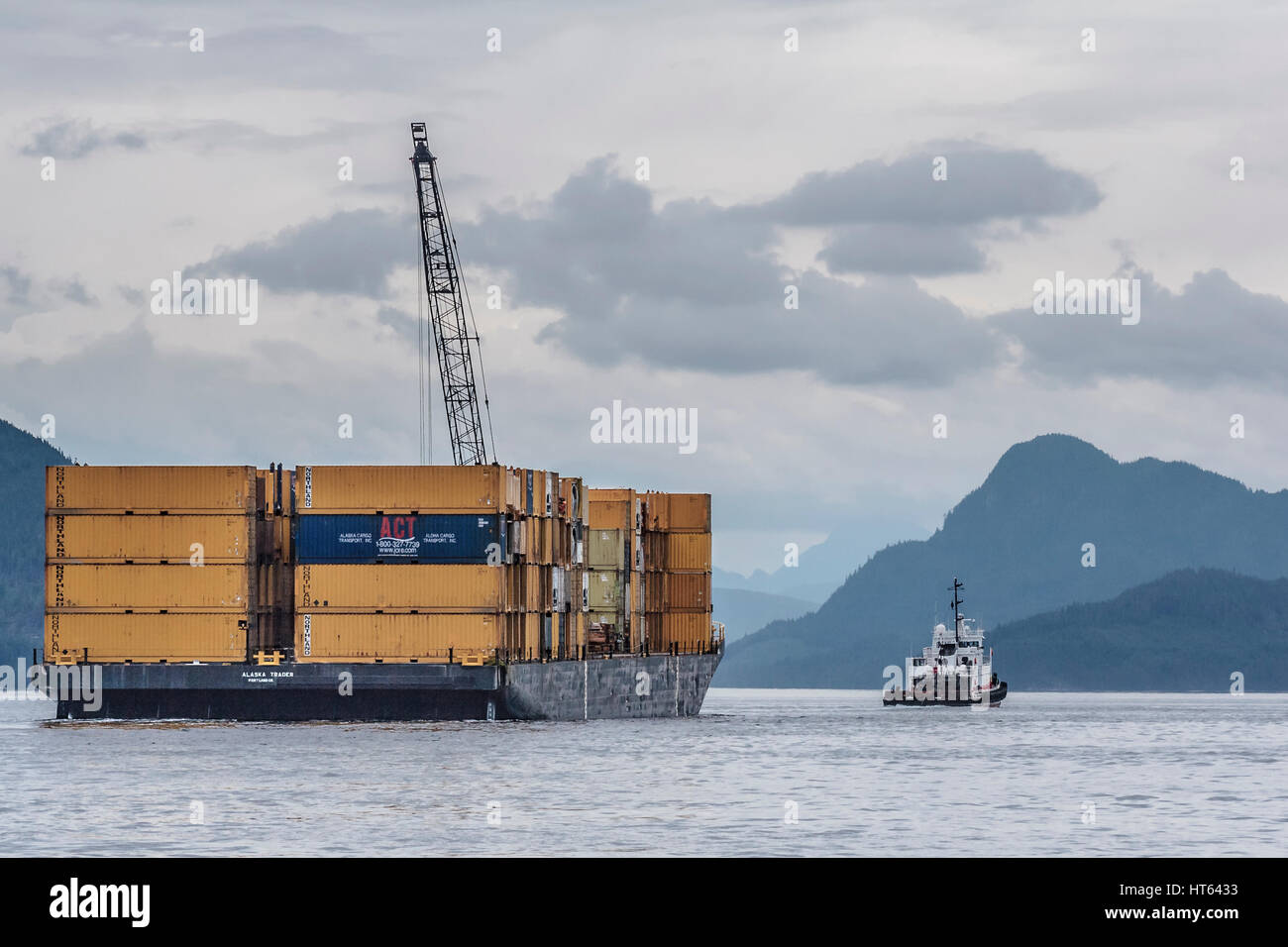 Ein Schlepper zieht ein Schiff beladen mit Containern und ausgestattet mit einem hohen Kran entlang Johnstone Strait, Teil von Britisch-Kolumbien Inside Passage. Stockfoto