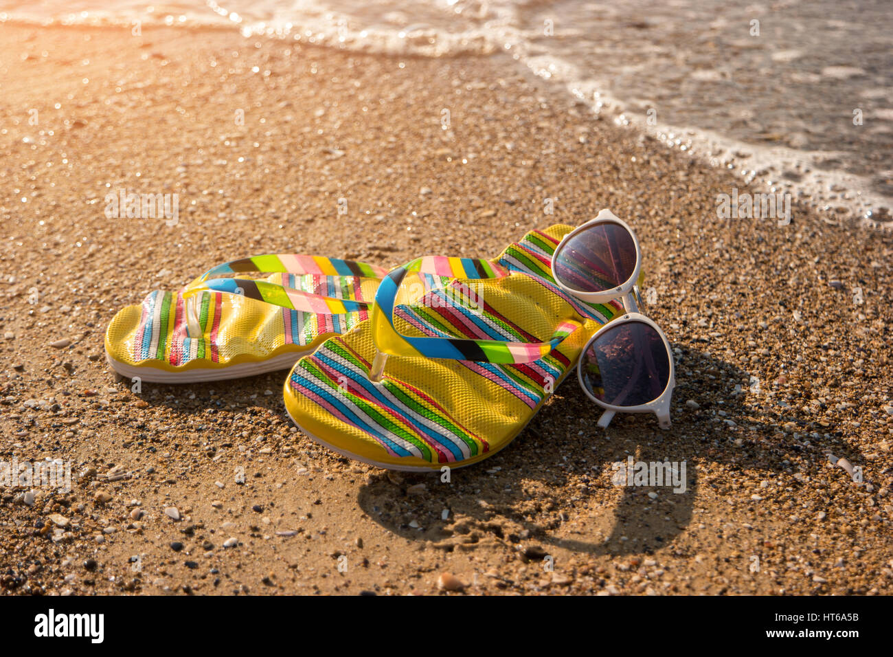 Flip Flops und Sonnenbrillen. Schuhe am Ufer. Höre den Ruf des Meeres. Verbringen Sie Sommer auf der tropischen Insel. Stockfoto