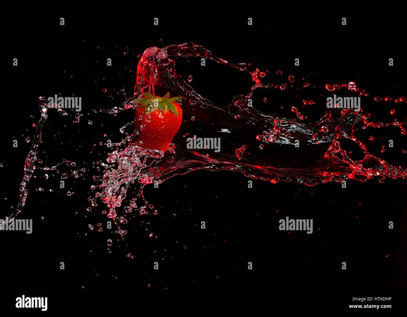 Hängende rote Erdbeere wird durch rotes Wasser spritzte Stockfoto