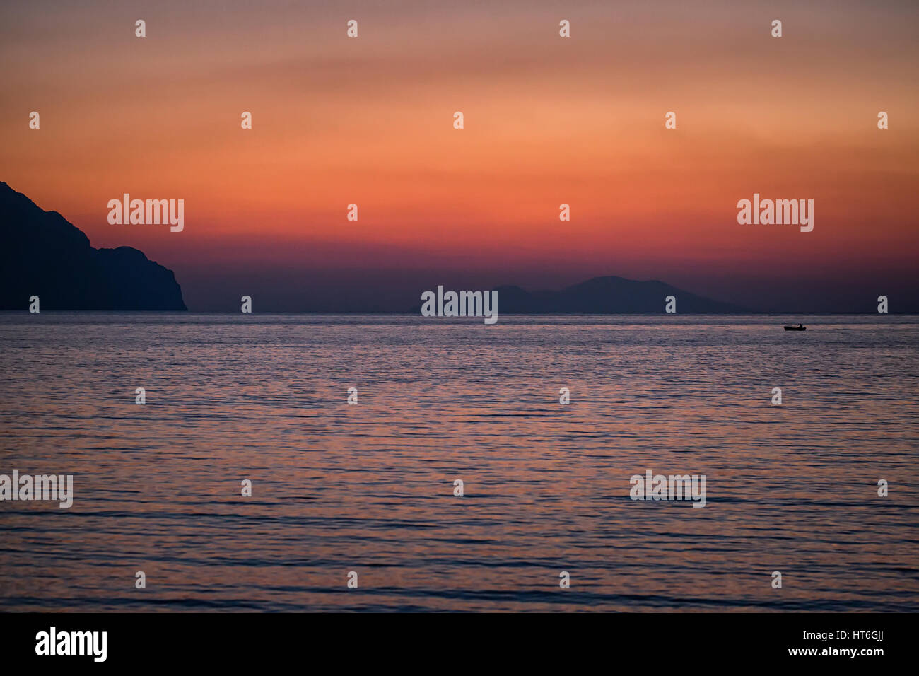 Kleines Boot Sonnenuntergang Silhouette ist ein Fischerboot paddeln entlang des Wassers mit einem bunten lila und rosa Nachthimmel im Hintergrund Stockfoto