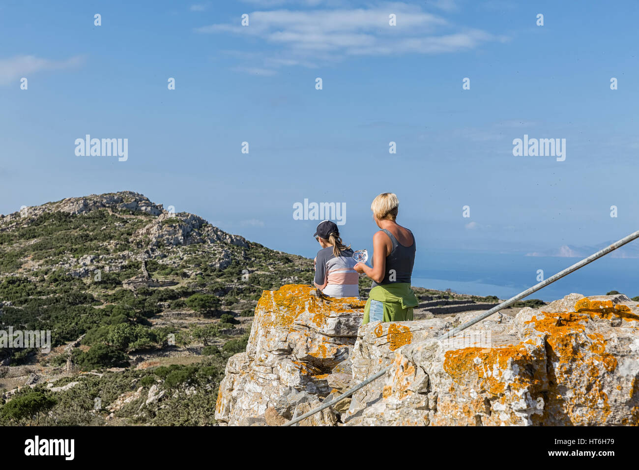 Zwei Frauen Essen einen Snack und bewundern Sie die wunderschöne Landschaft Blick auf die grünen Berge, Amorgos Island, Griechenland Stockfoto