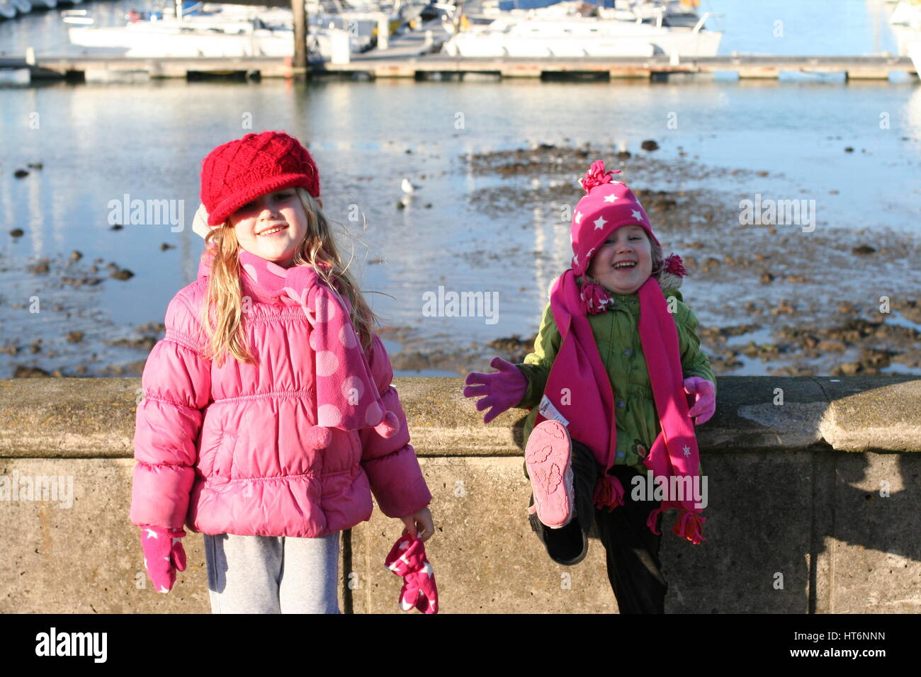Zwei Mädchen, Kinder verwirren und Tanzen durch den Hafen Wand an einem kalten und windigen Tag, Howth, Dublin, Irland Stockfoto