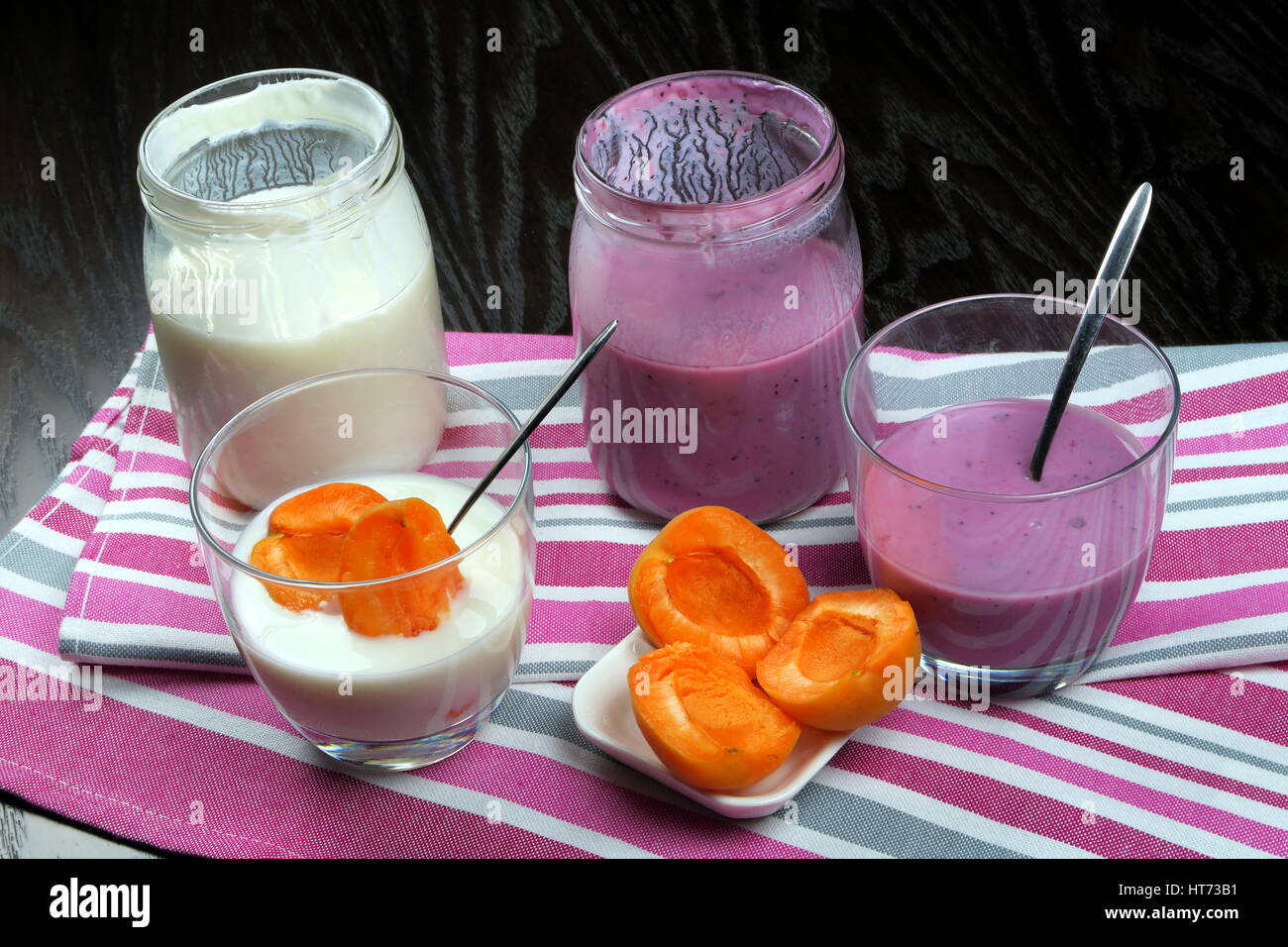 Hausgemachte Bio fettarmer schlicht und Heidelbeer Joghurt in einem klaren Glas (und Glas) mit Teelöffel und Aprikosen auf bunte Küchentücher Stockfoto