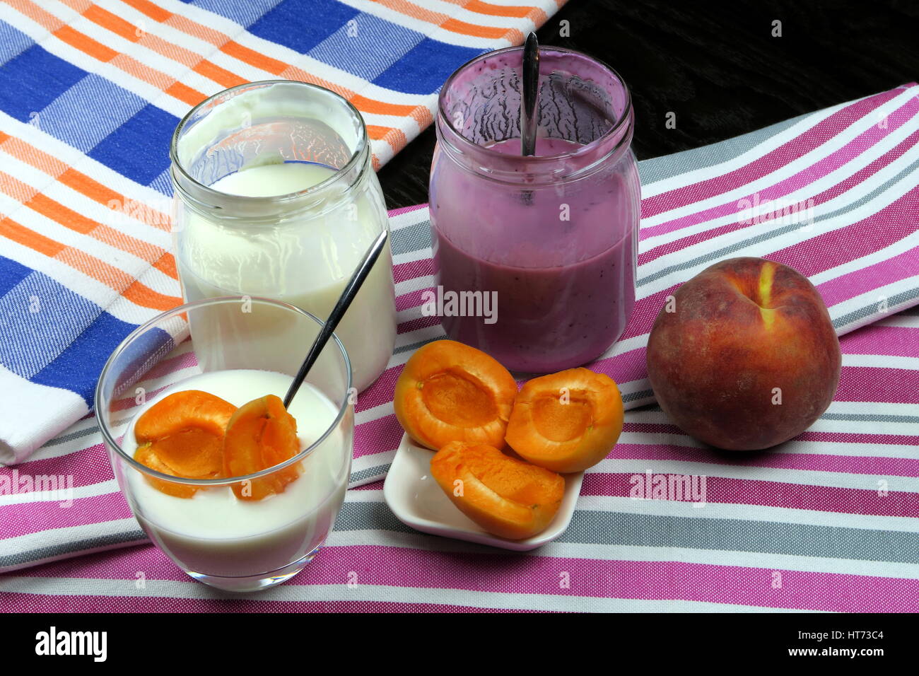 Hausgemachte Bio fettarmer schlicht und Heidelbeer Joghurt in einem klaren Glas (und Glas) mit TL, Aprikosen und Pfirsich auf bunte Küchentücher Stockfoto