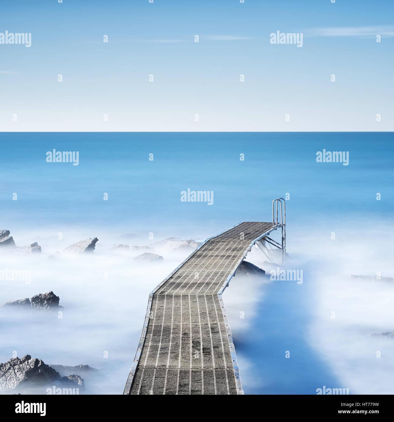 Pier oder Steg und Felsen auf einem blauen Ozean am Morgen. Langzeitbelichtung Stockfoto