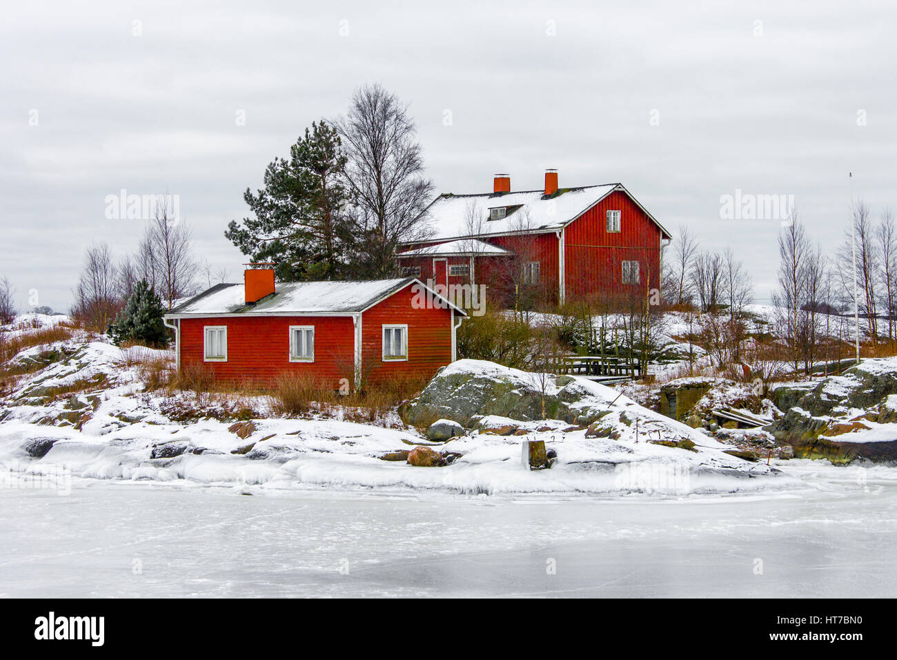 Rotes Holzhaus auf einer Insel von Wasser umgeben und bedeckt in Schnee und Eis im Winter in Helsinki, Finnland. Stockfoto