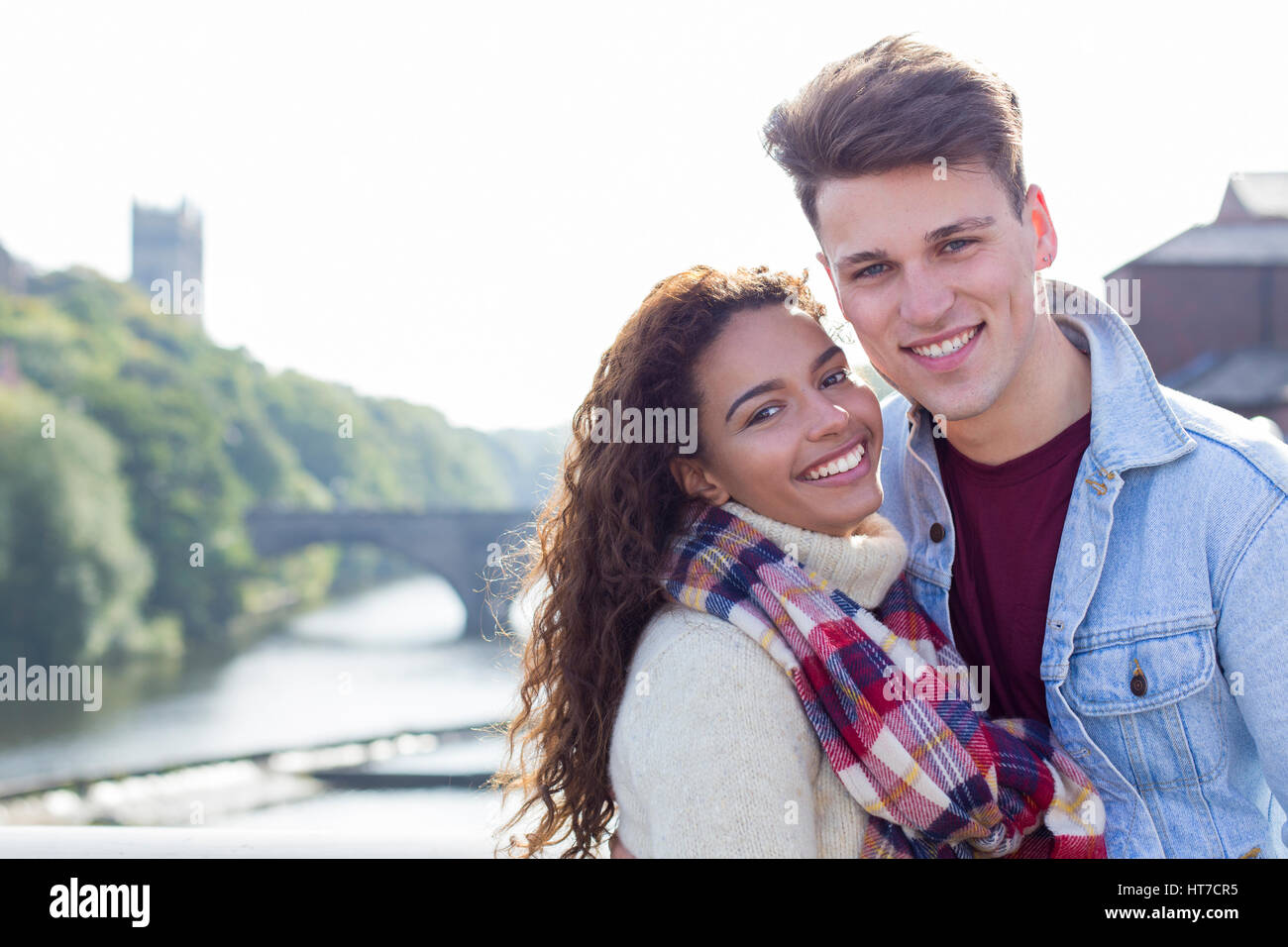 Ein glückliches junges Paar mit einem Lächeln in die Kamera entspannen sie im Freien am Fluss. Sie sind für den Winter Warm verpackt. Stockfoto
