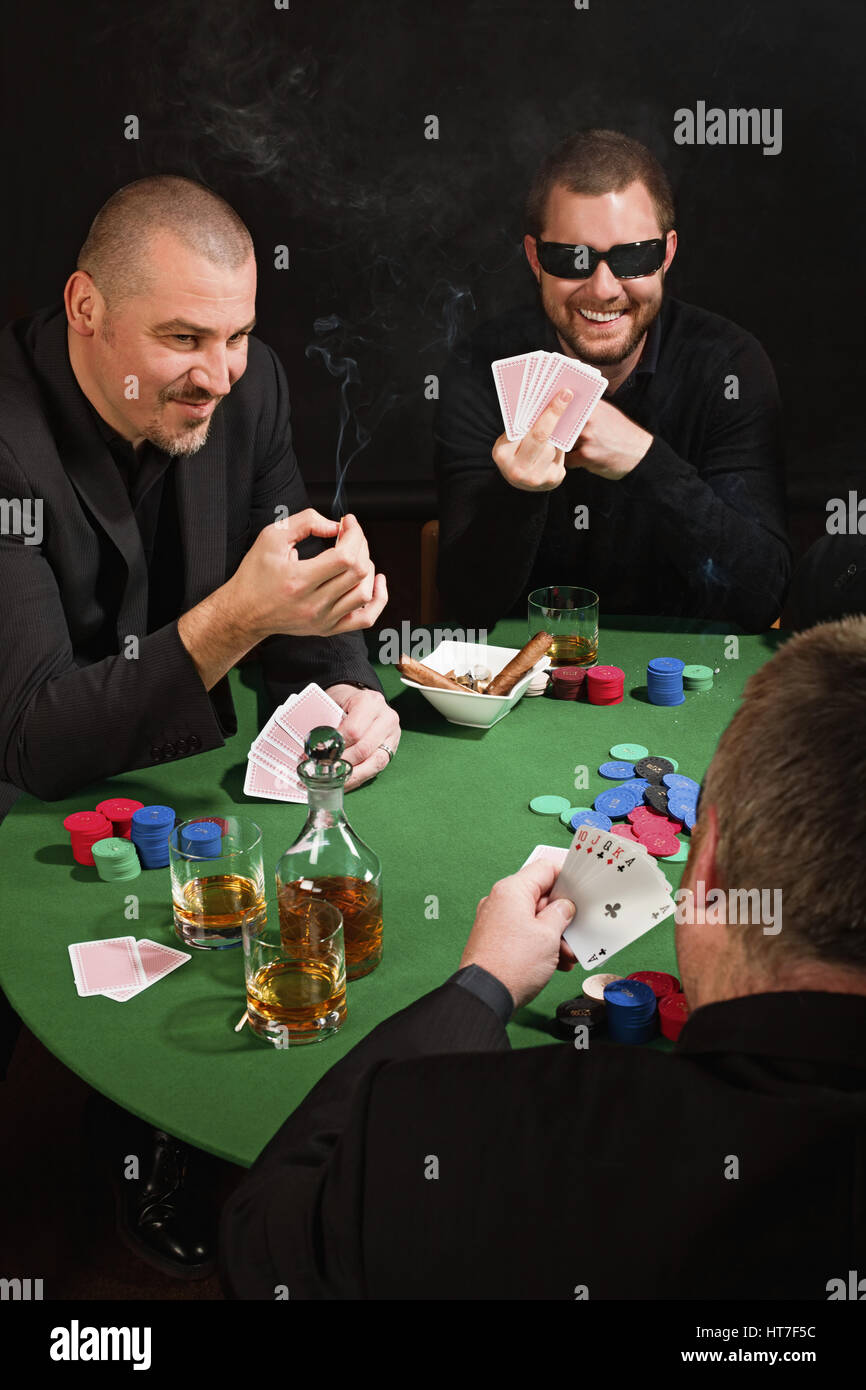Foto von drei Männern Pokern, Zigarren rauchen, trinken Whisky und einer spiegeln den Vogel an den Spieler mit der gute Pokerhand. Stockfoto