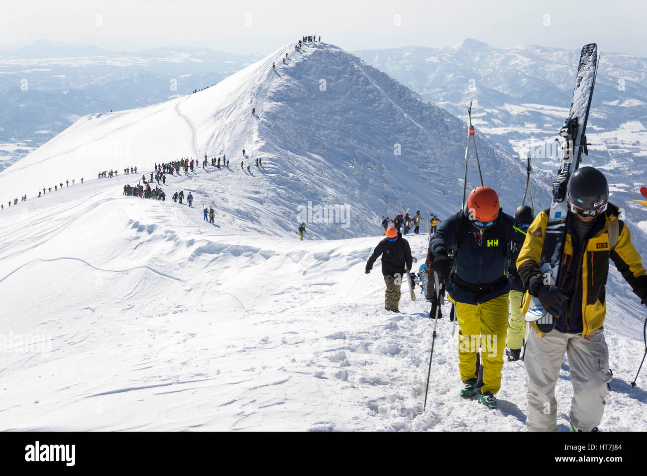 Linie von Skifahrern und Snowboardern Wandern Out Of Bounds Skistation In Niseko an einem sonnigen Tag Stockfoto