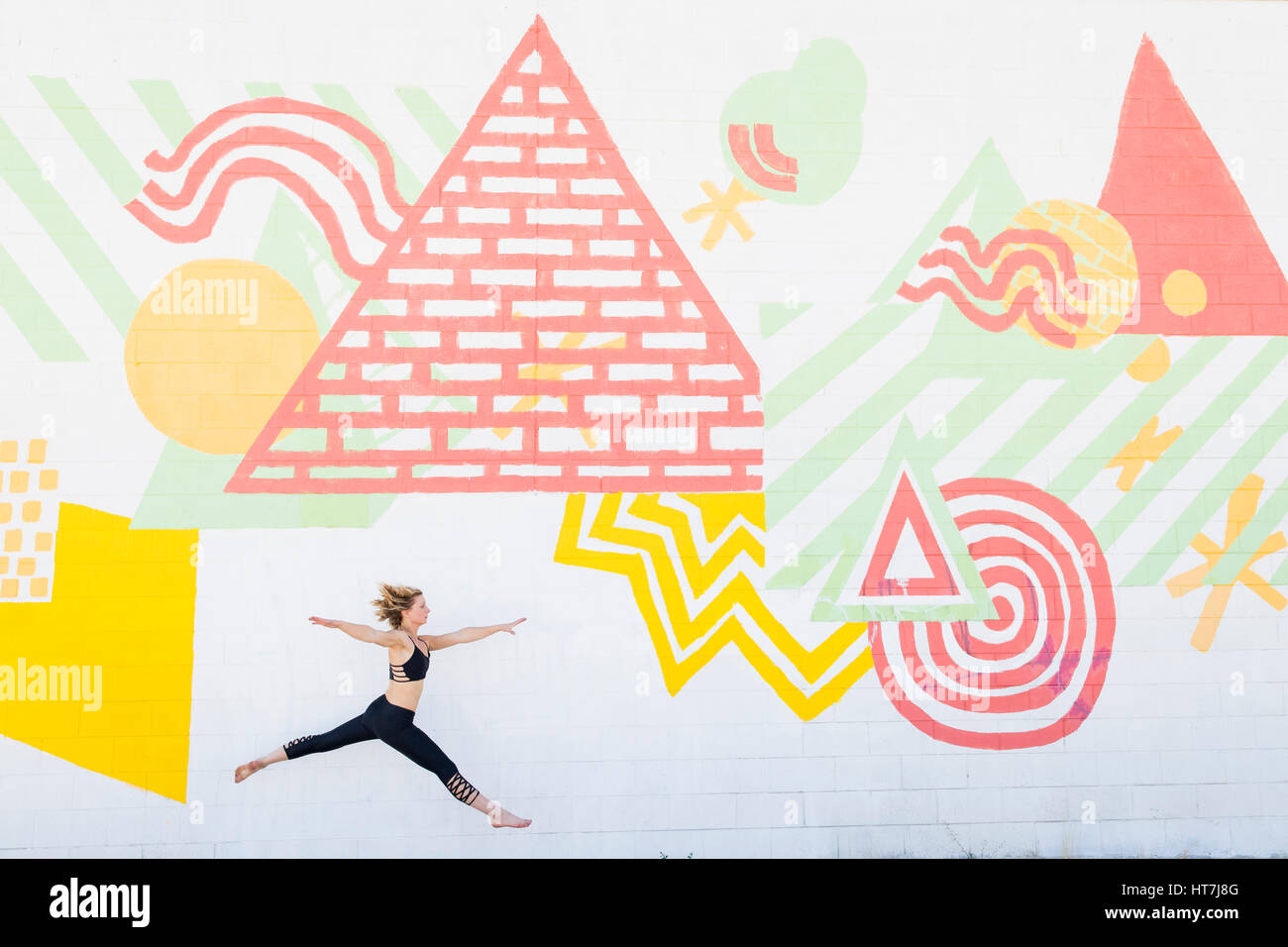 Eine Frau springt In die Luft vor einer Wand von Street Art Stockfoto