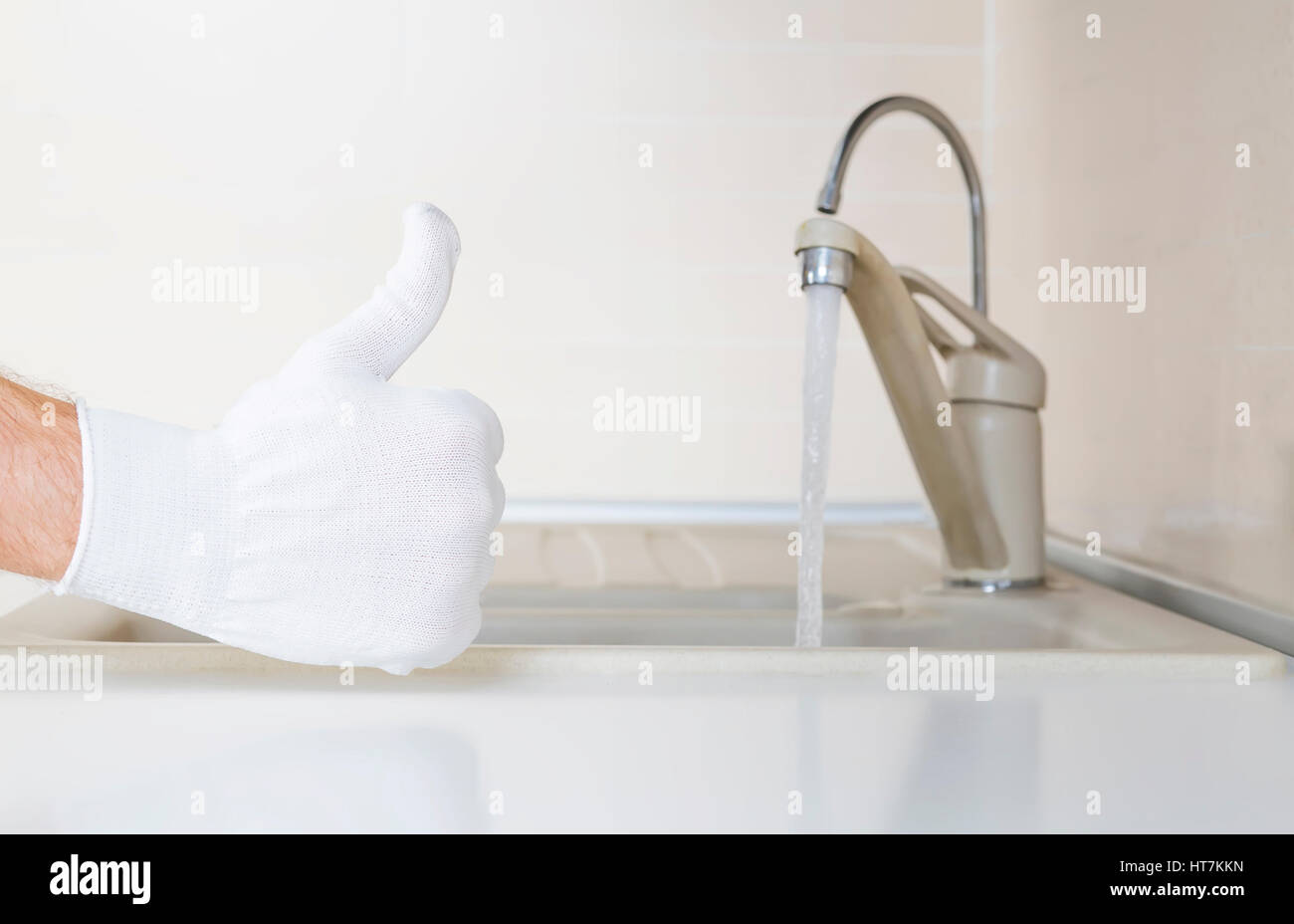 Klempner Hand mit Daumen oben auf Küche Hintergrund. Klempner auftauchend Daumen auf neuen Tippen Sie auf Hintergrund. Gute Sanitär Reparaturen. Stockfoto