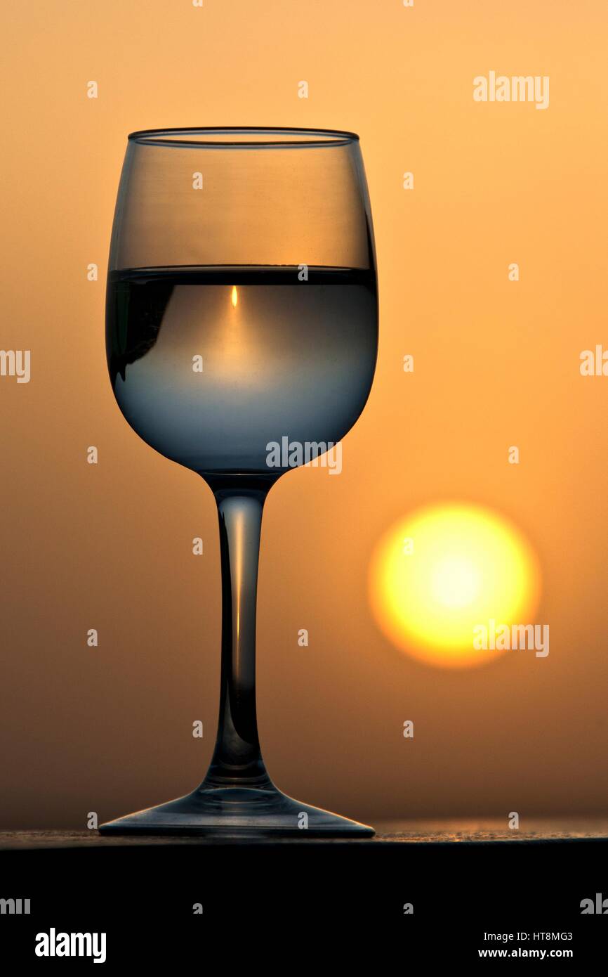 Ein Glas Weißwein mit dem goldenen Sonnenuntergang und die Landschaft, die durch ihn gebrochen. Stockfoto