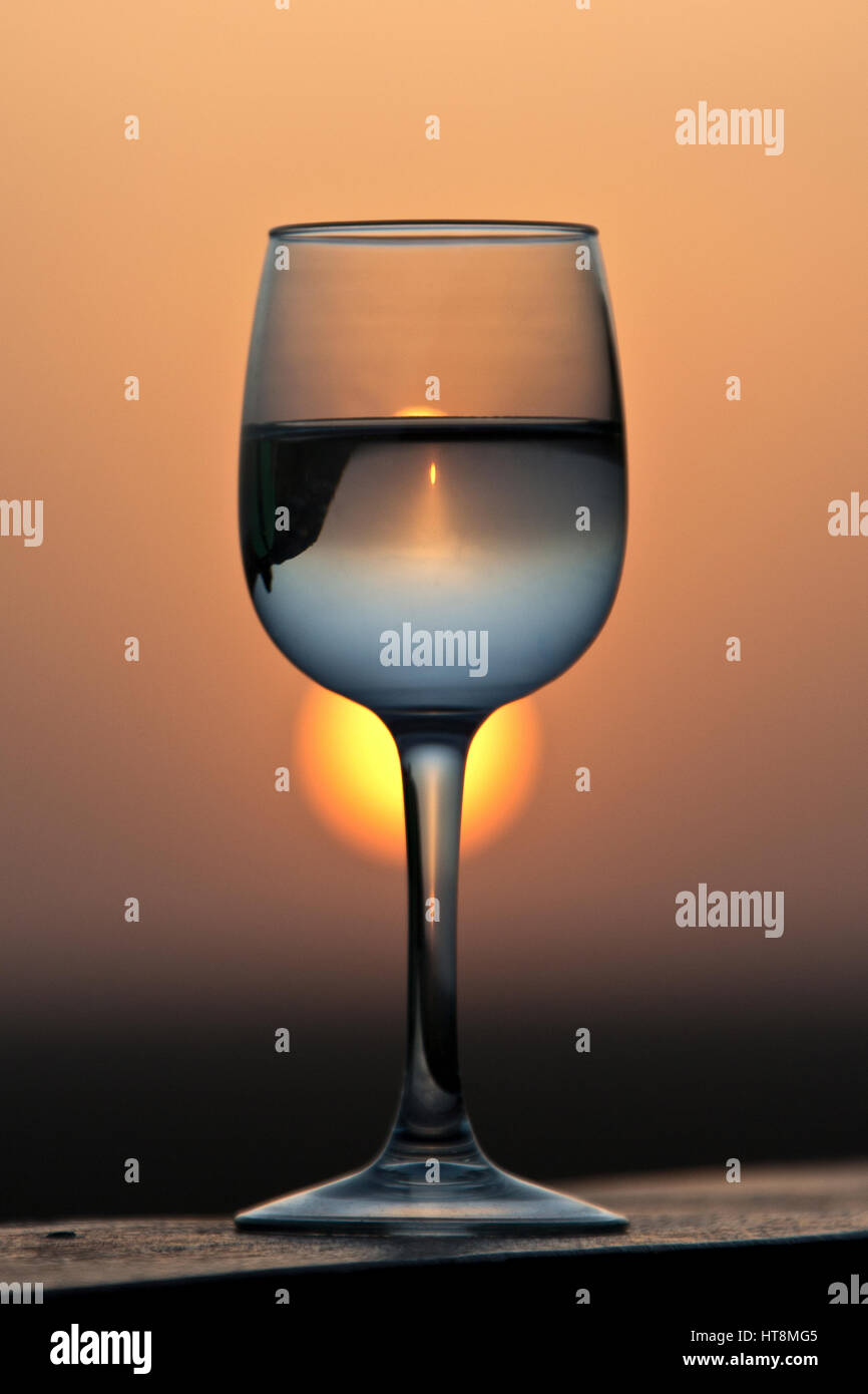 Ein Glas Weißwein mit dem goldenen Sonnenuntergang und die Landschaft, die durch ihn gebrochen. Stockfoto