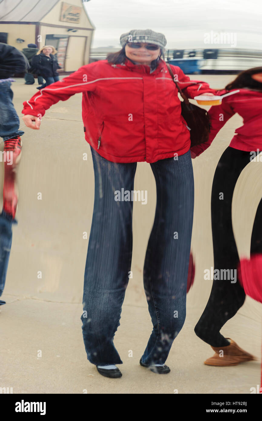 Das Bild einer Frau mittleren Alters mit roter Jacke spiegelt sich auf der Oberfläche eines verzerrenden Spiegels am Navy Pier in Chicago, Illinois. Stockfoto
