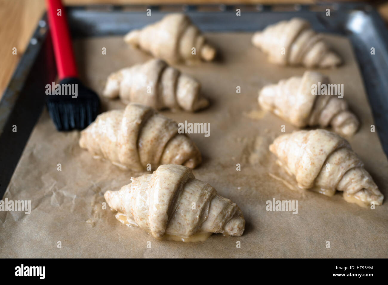 Vollkorn-Croissants machen und Bürsten mit Ei auf Backblech mit Backpapier drauf Stockfoto