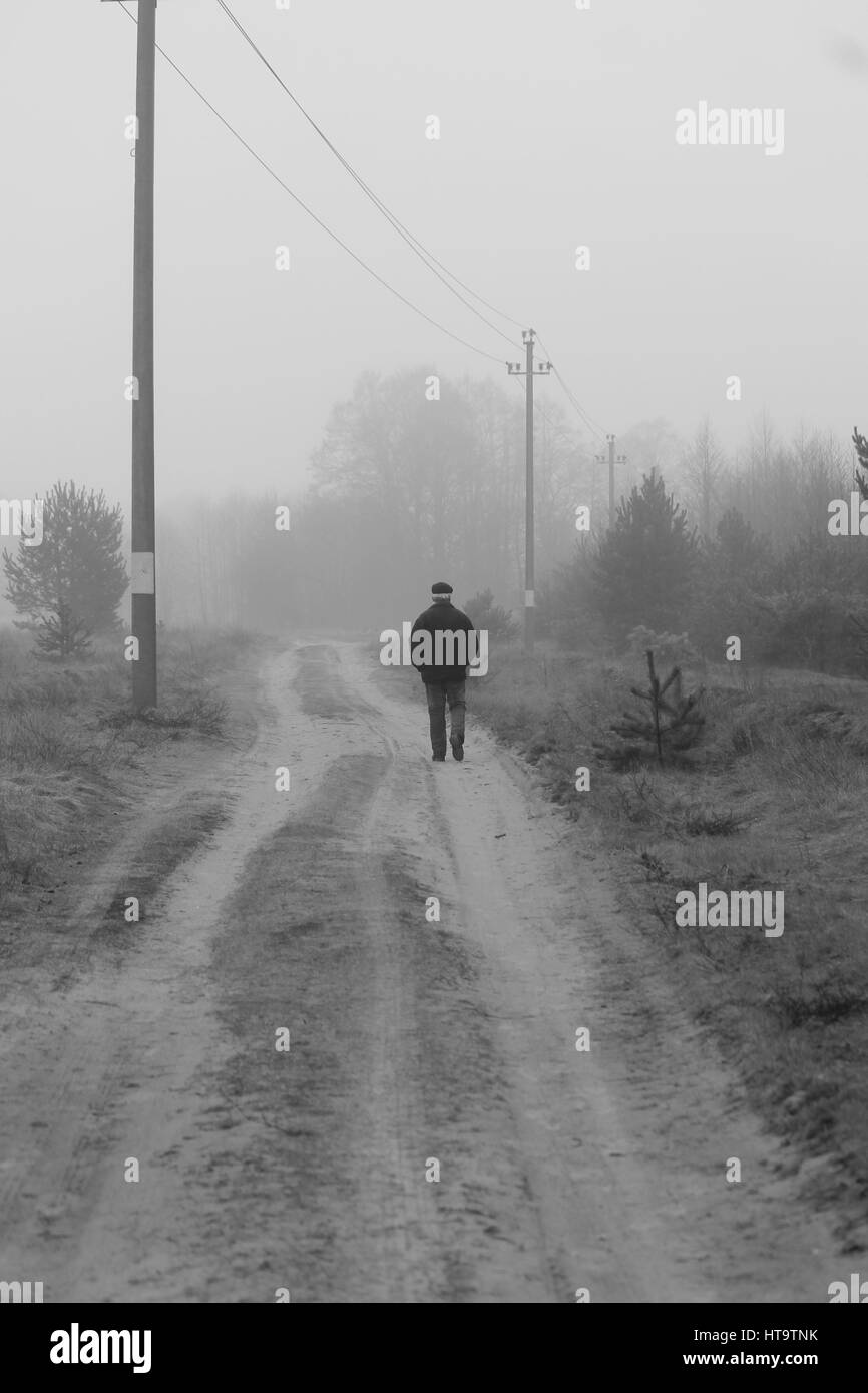 einsame Figur Mann zu Fuß auf der Landstraße abgedeckt milchigen dichten Nebel Stockfoto