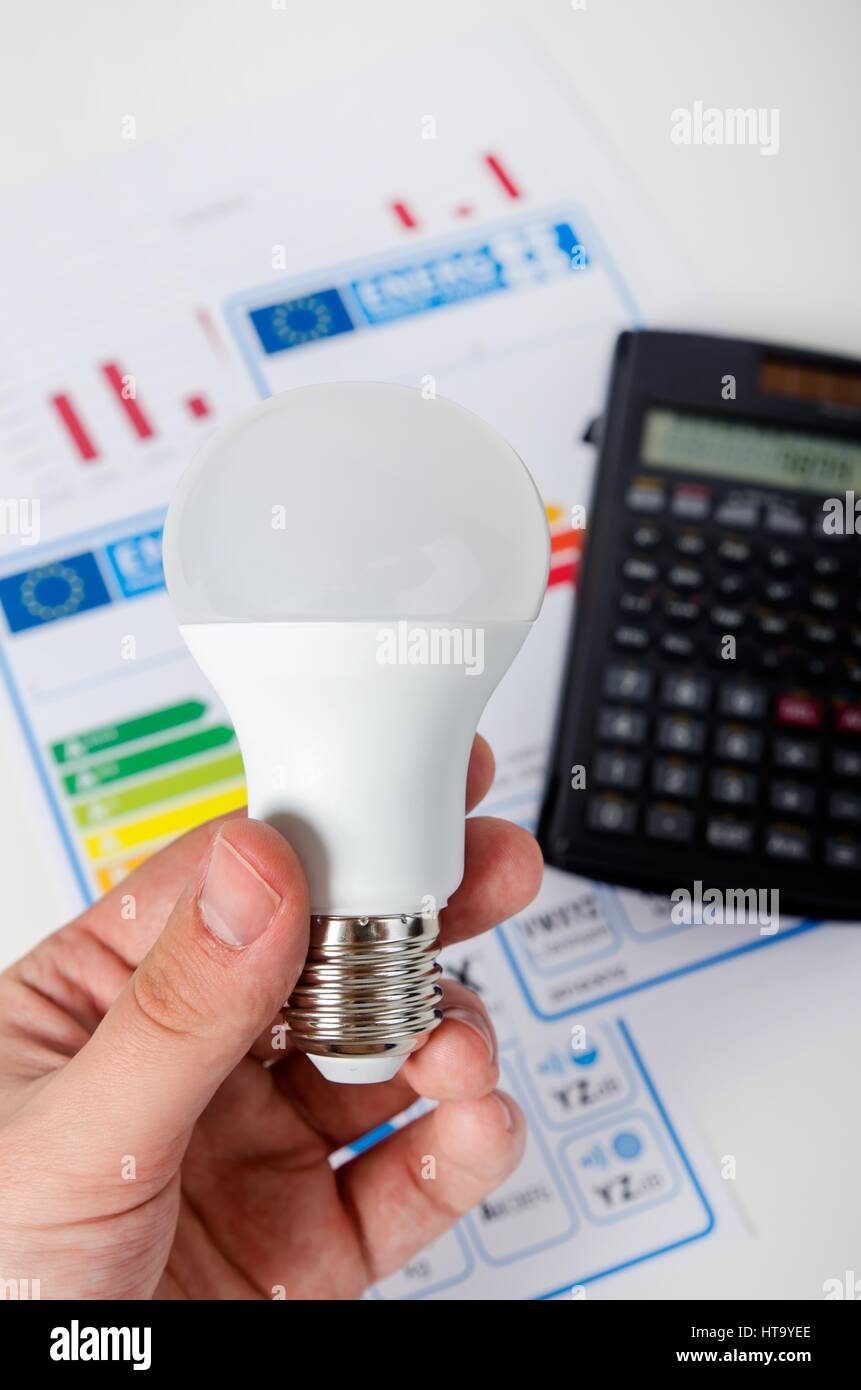 Hand halten LED Leuchtmittel. Energie-Effizienz-Diagramm und Rechner im Hintergrund Stockfoto