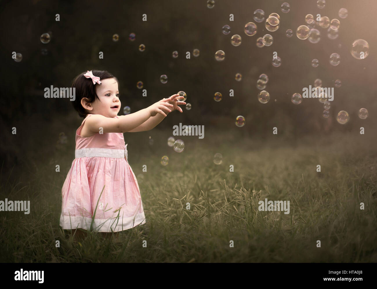 Ein kleines Mädchen steht und versucht, eine Seifenblase, umgeben von vielen Bläschen zu fangen Stockfoto