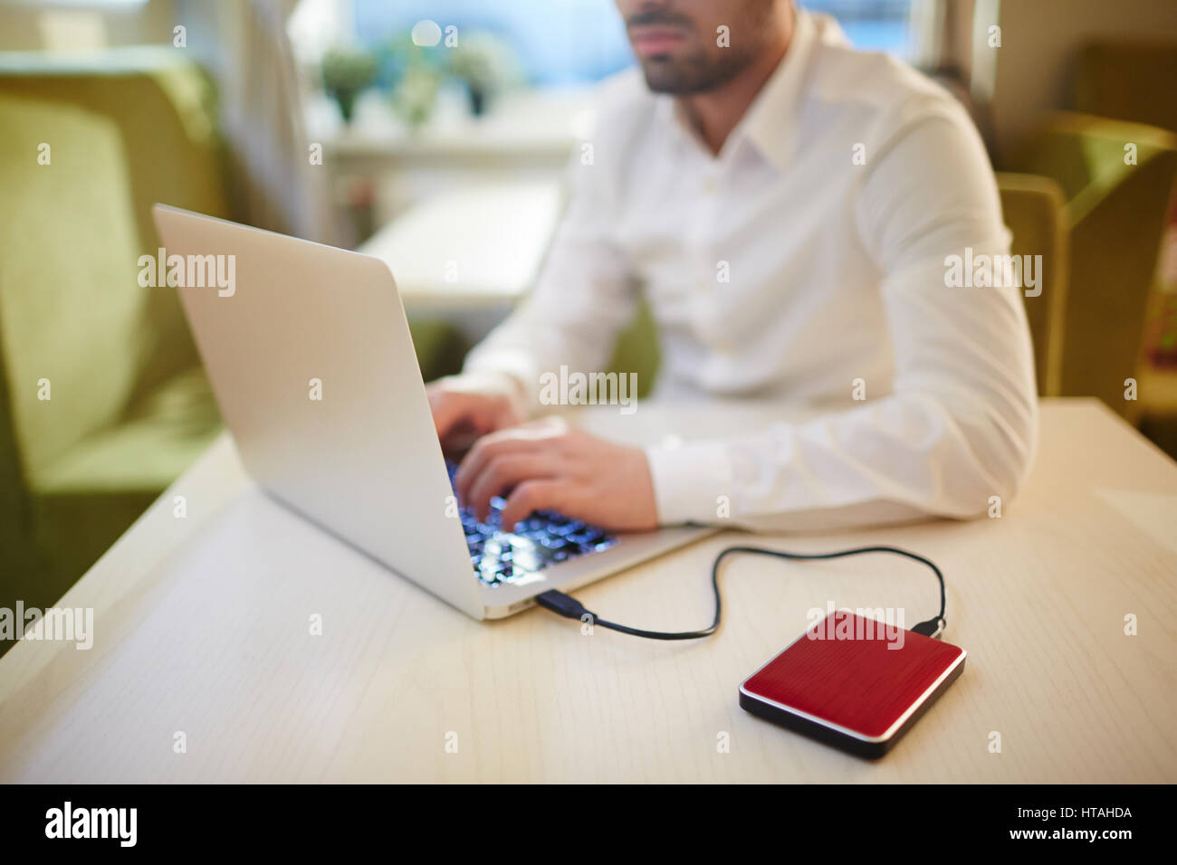 Ernsthafte bärtigen Journalist im Internetcafé sitzen und schreiben Artikel für das Magazin auf Laptop angeschlossen auf externe Festplatte Stockfoto