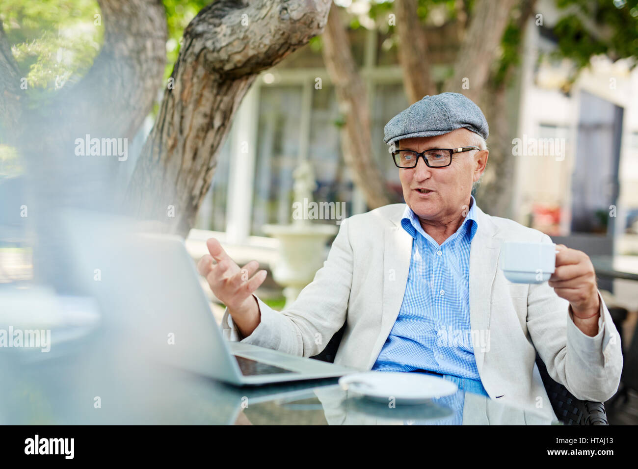 Porträt des modernen Rentner emotional gestikulieren, wenn man etwas überraschend auf dem Bildschirm des Laptops während der Morgenstunden der Ruhe und das Frühstück im Stockfoto