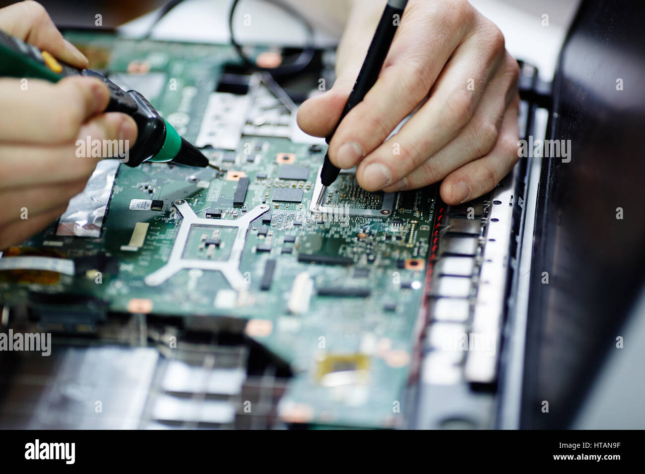 Closeup Aufnahme von männlichen Händen testen elektrischen Strom in Platine zerlegt Laptop mit multimeter Werkzeug auf Tabelle in Werkstatt Stockfoto