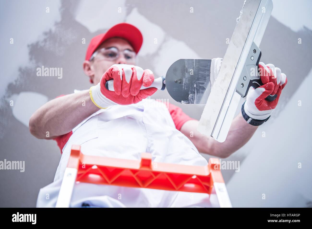 Professionelle kaukasischen Bau und Umbau Arbeiter, die Vorbereitung für den Trockenbau Patchen mischen Joint Gummimischungen während Ihres Aufenthalts auf der Leiter. Stockfoto